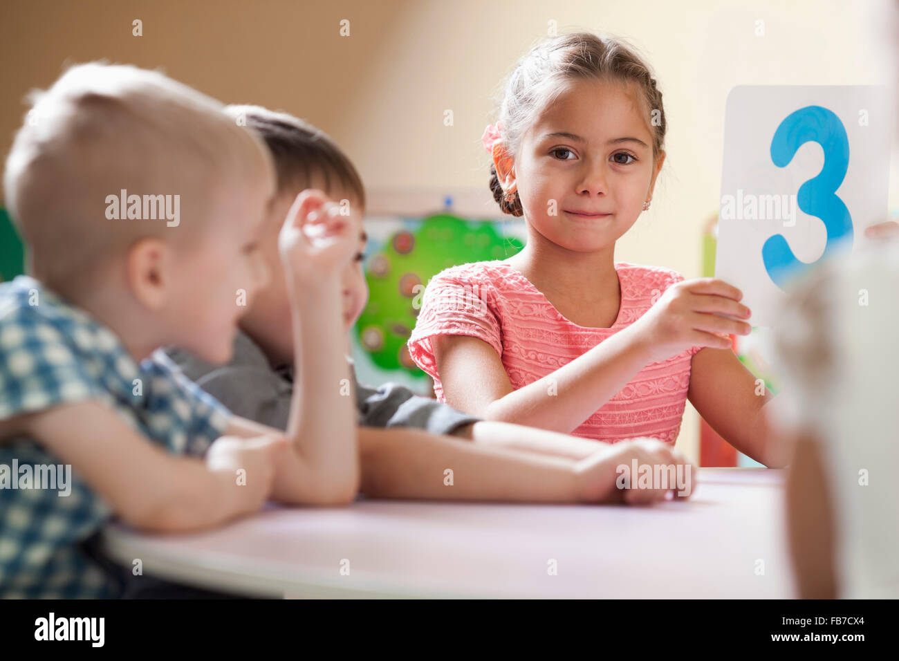 Porträt von netten Mädchen halten Nummer 3 Plakat beim sitzen neben Freunden im Klassenzimmer Stockfoto