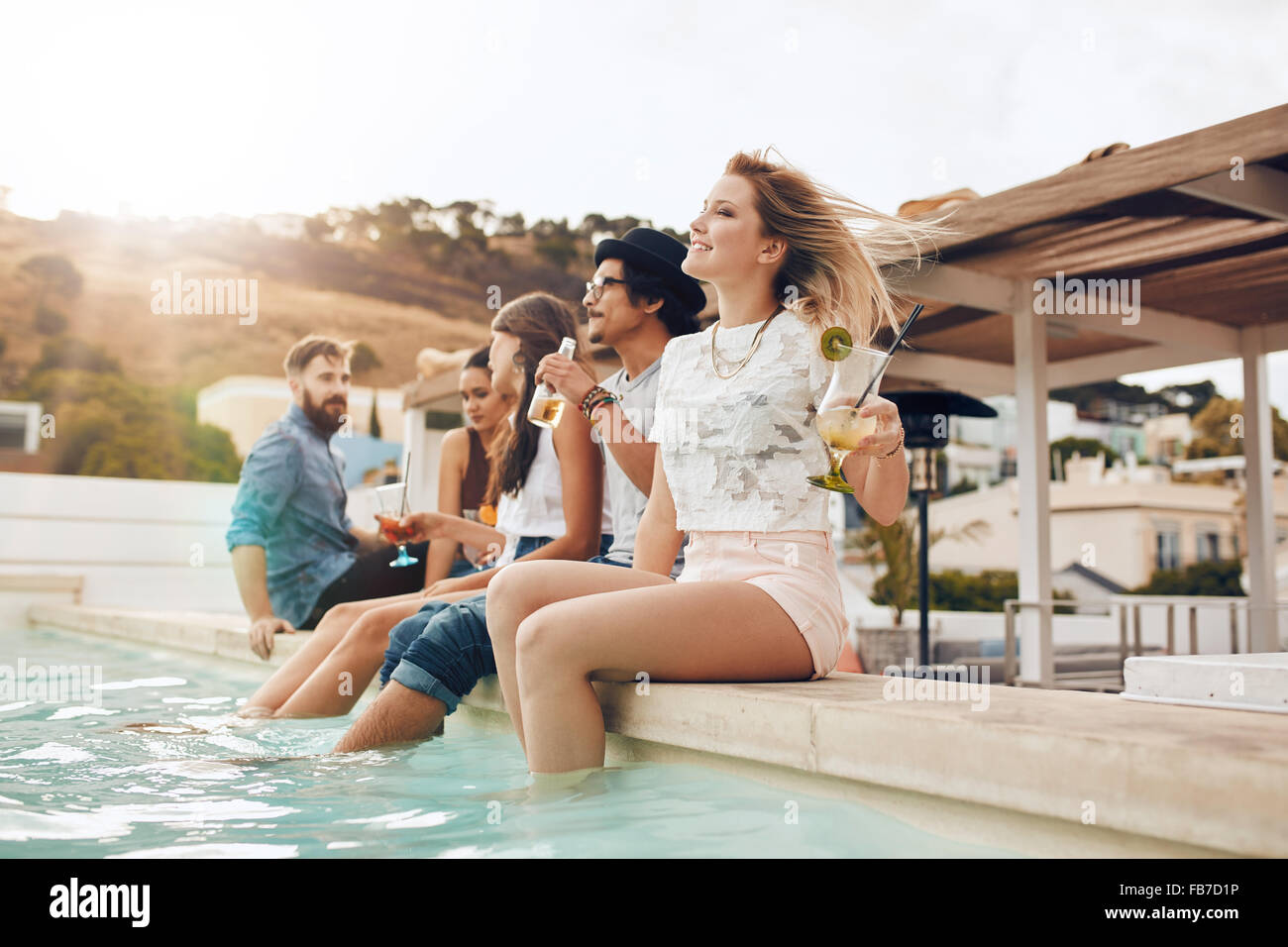 Porträt der jungen Menschen sitzen am Rand des Schwimmbades mit den Füßen im Wasser. Freunden entspannen am Pool während Stockfoto