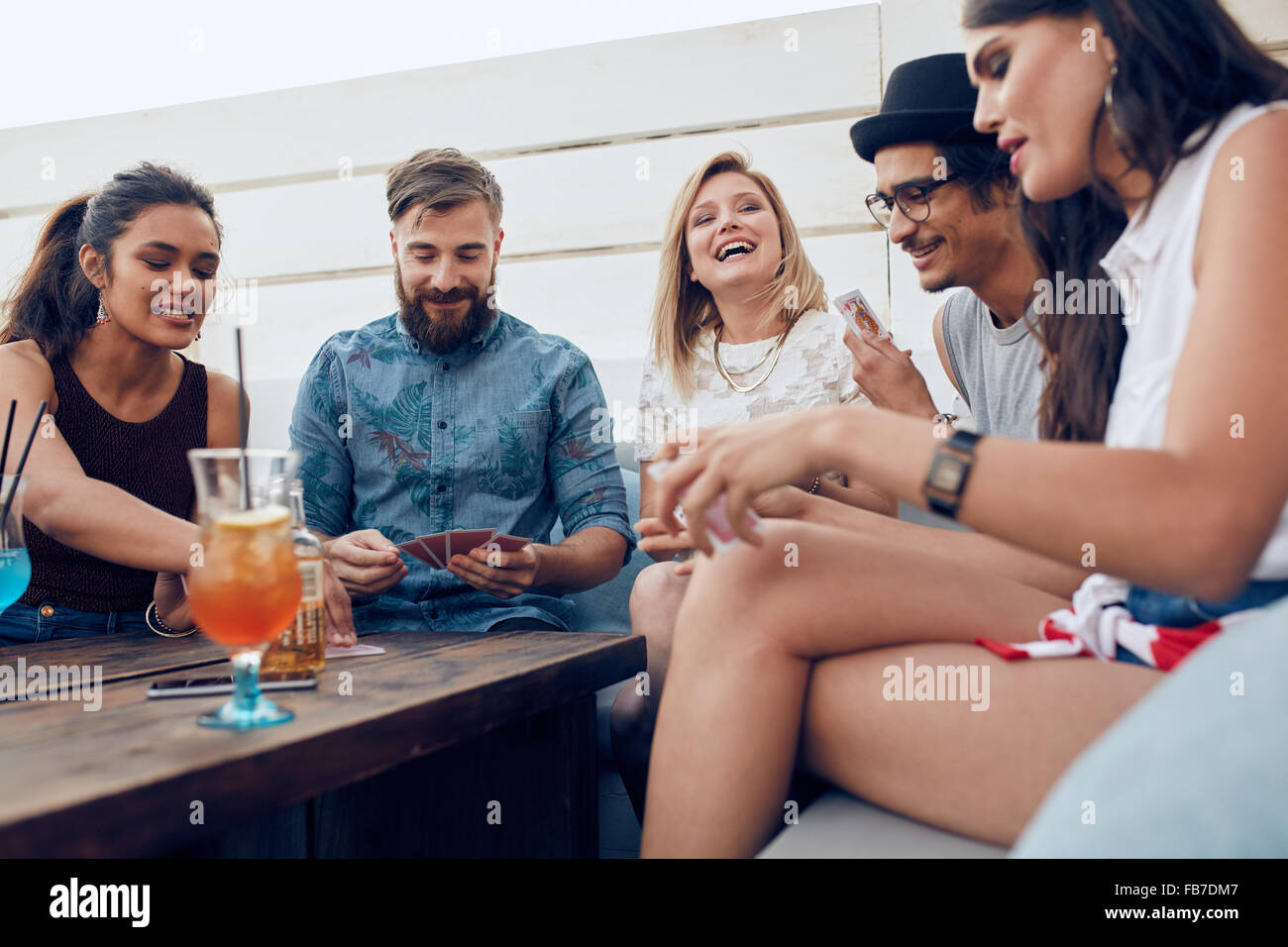 Gruppe von Freunden sitzen an einem Holztisch und Spielkarten. Fröhliche junge Menschen feiern zusammen und spielen Karten. Stockfoto