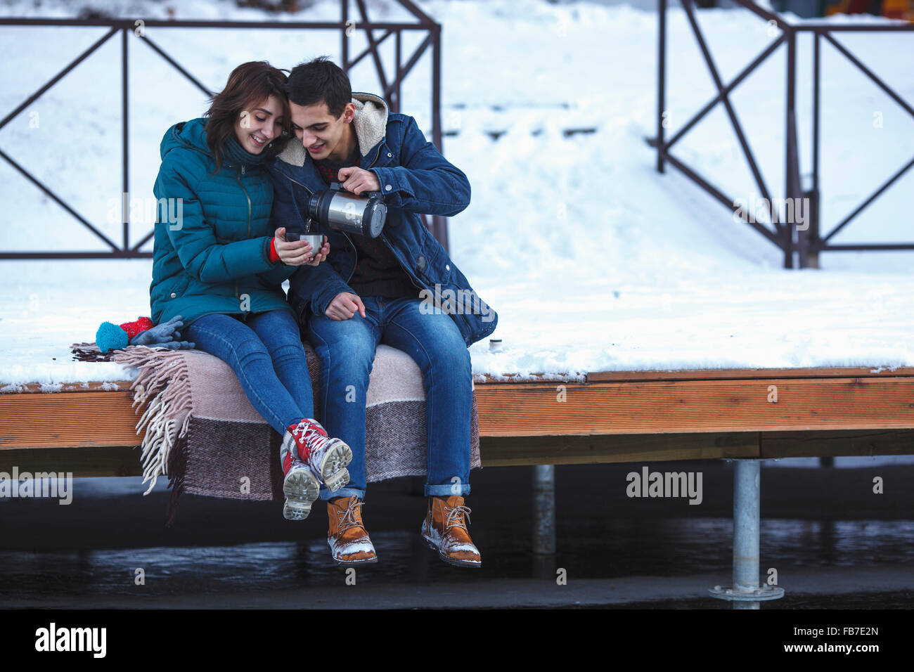 Voller Länge des jungen Mannes mit Kaffee Freundin sitzen am pier Stockfoto