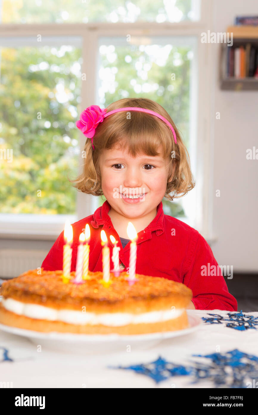 Glückliches Mädchen Blick auf Geburtstagskuchen auf Tisch Stockfoto