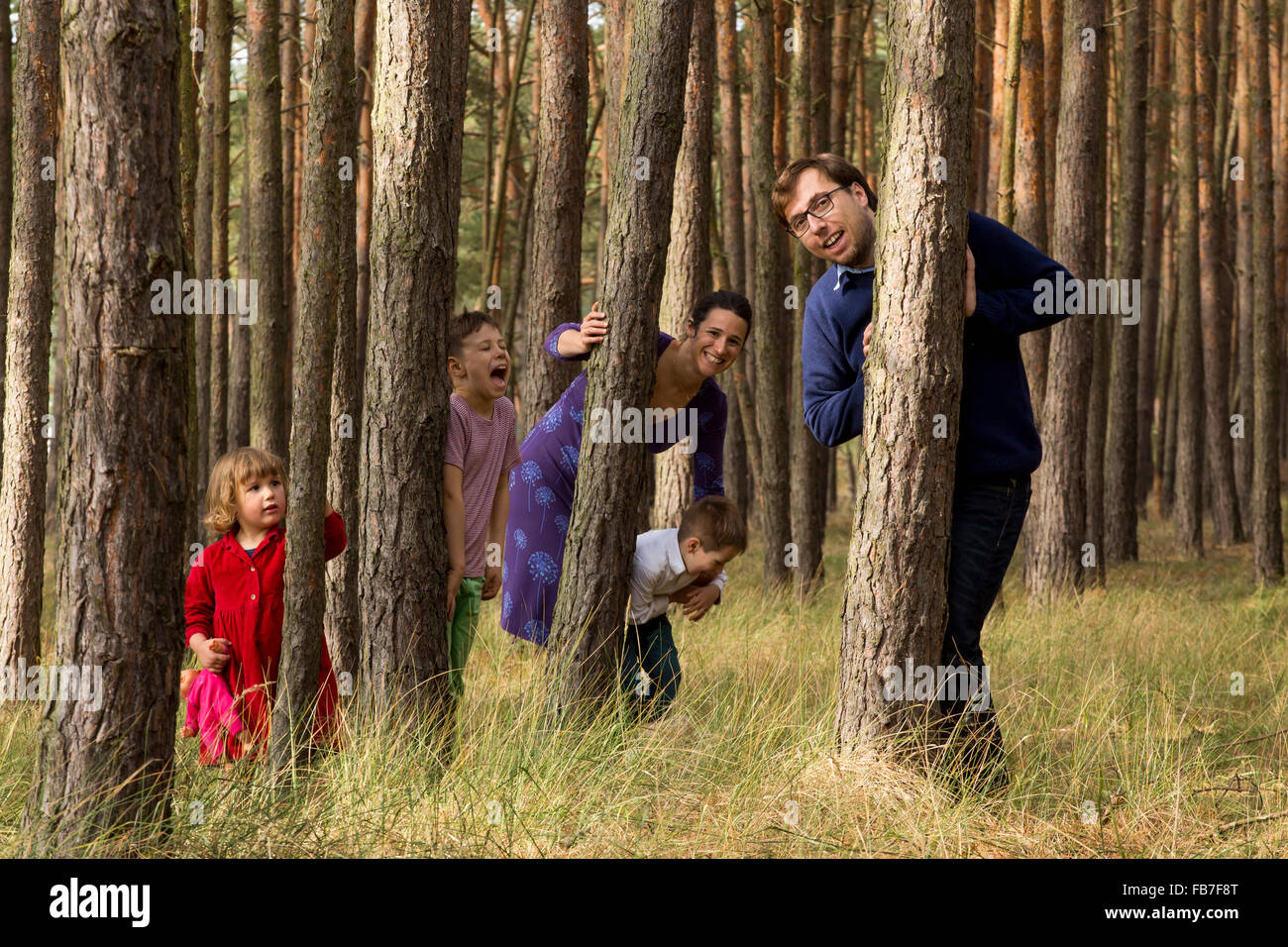 Glückliche Familie versteckt sich hinter Baumstämmen im Wald Stockfoto