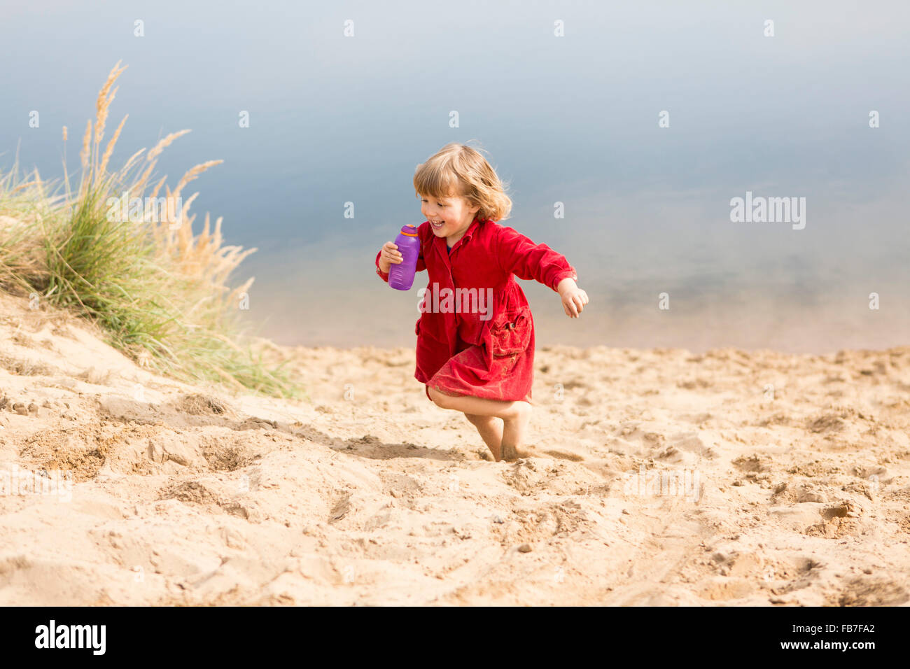 Fröhliches Mädchen mit Wasser Flasche beim laufen auf Sand dune Stockfoto