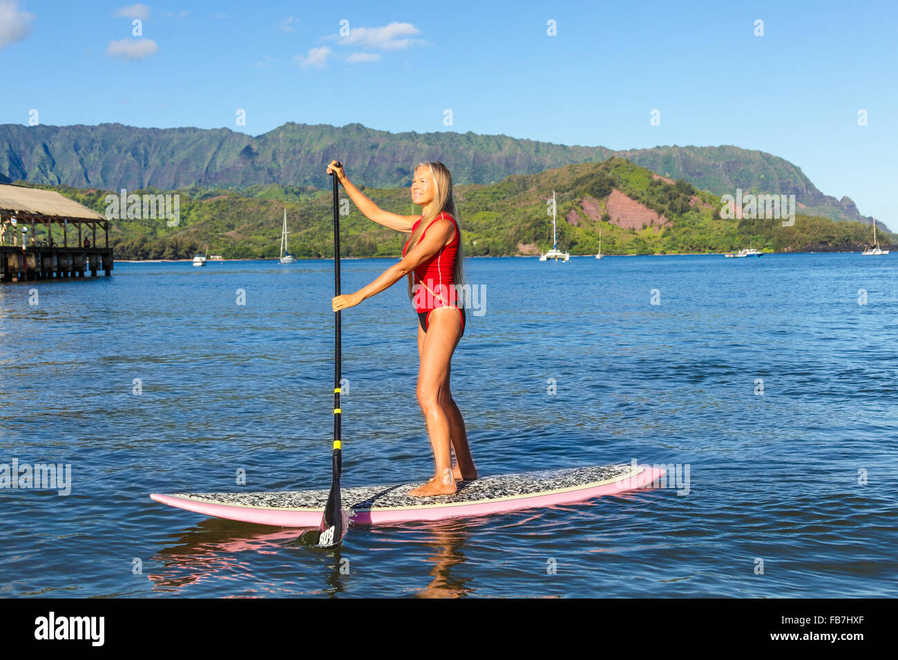 Frau auf Stand up Paddle Board in Hanalei Bay, mit Mt. Makana genannt Bali Hai und Hanalei Pier im Hintergrund Stockfoto