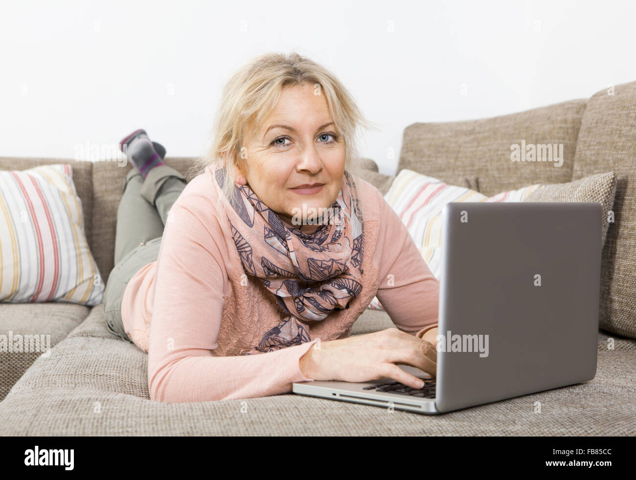 eine ältere blonde Frau auf dem Sofa liegen und arbeiten mit einem laptop Stockfoto