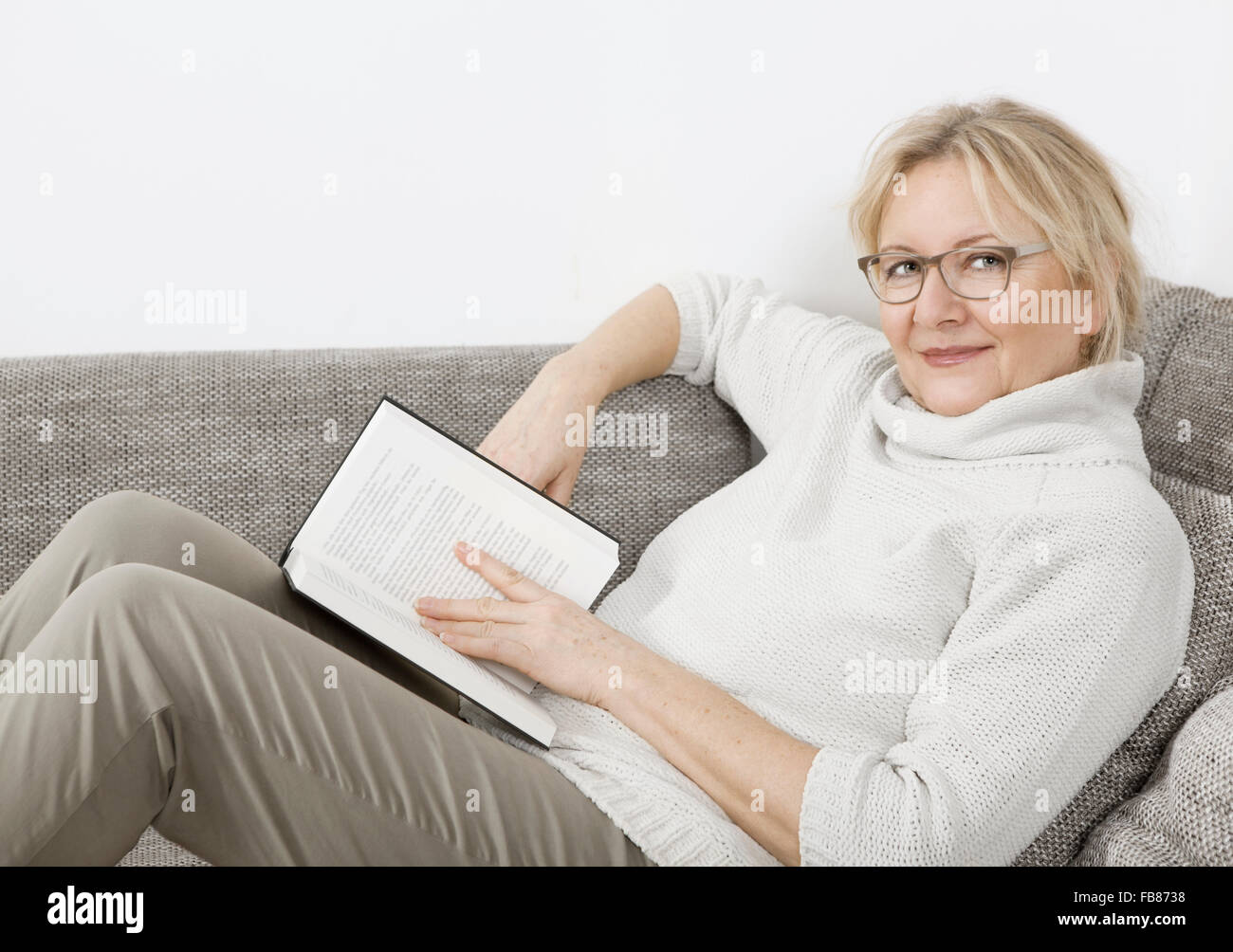 eine ältere blonde Frau auf dem Sofa liegen und ein Buch zu lesen Stockfoto