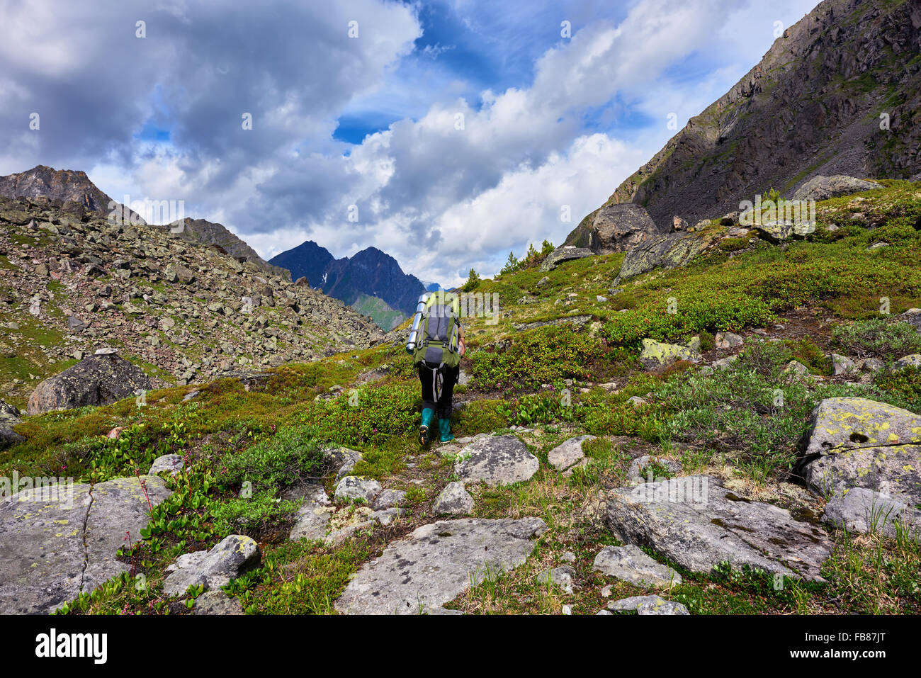 Wandern. Bergtourismus. Eine Frau mit einem großen Rucksack in Gummistiefeln geht auf einem Bergpfad Stockfoto