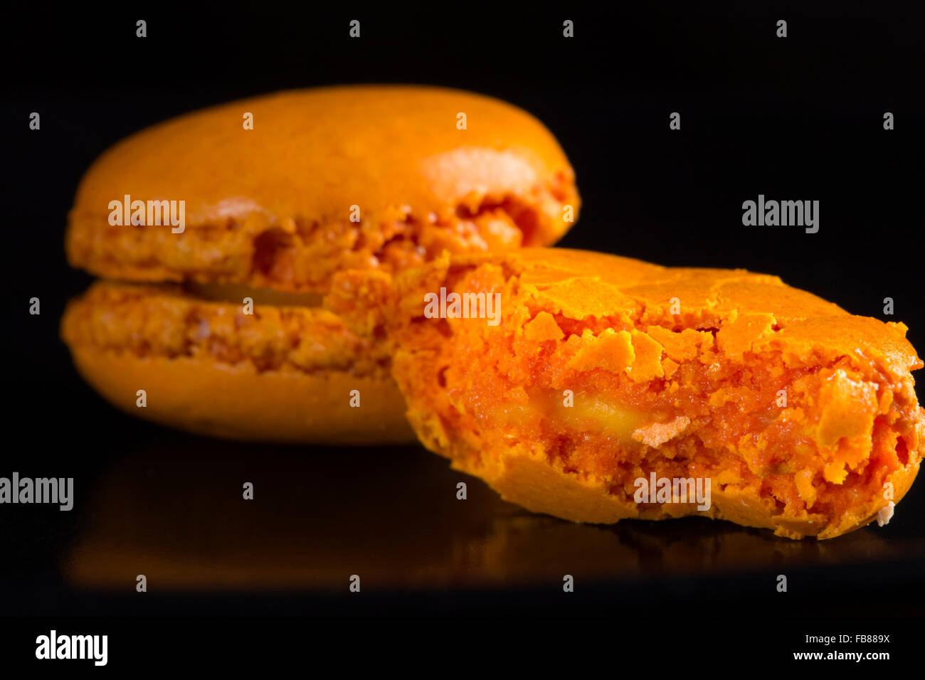 Nahaufnahme einer gebissen orange Makronen auf schwarzem Hintergrund Stockfoto