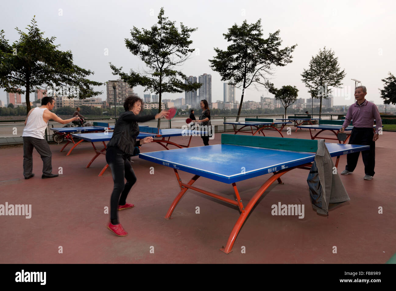 Menschen spielen in einem Park am Flussufer bei einer typischen Stadt in China Tischtennis. Stockfoto