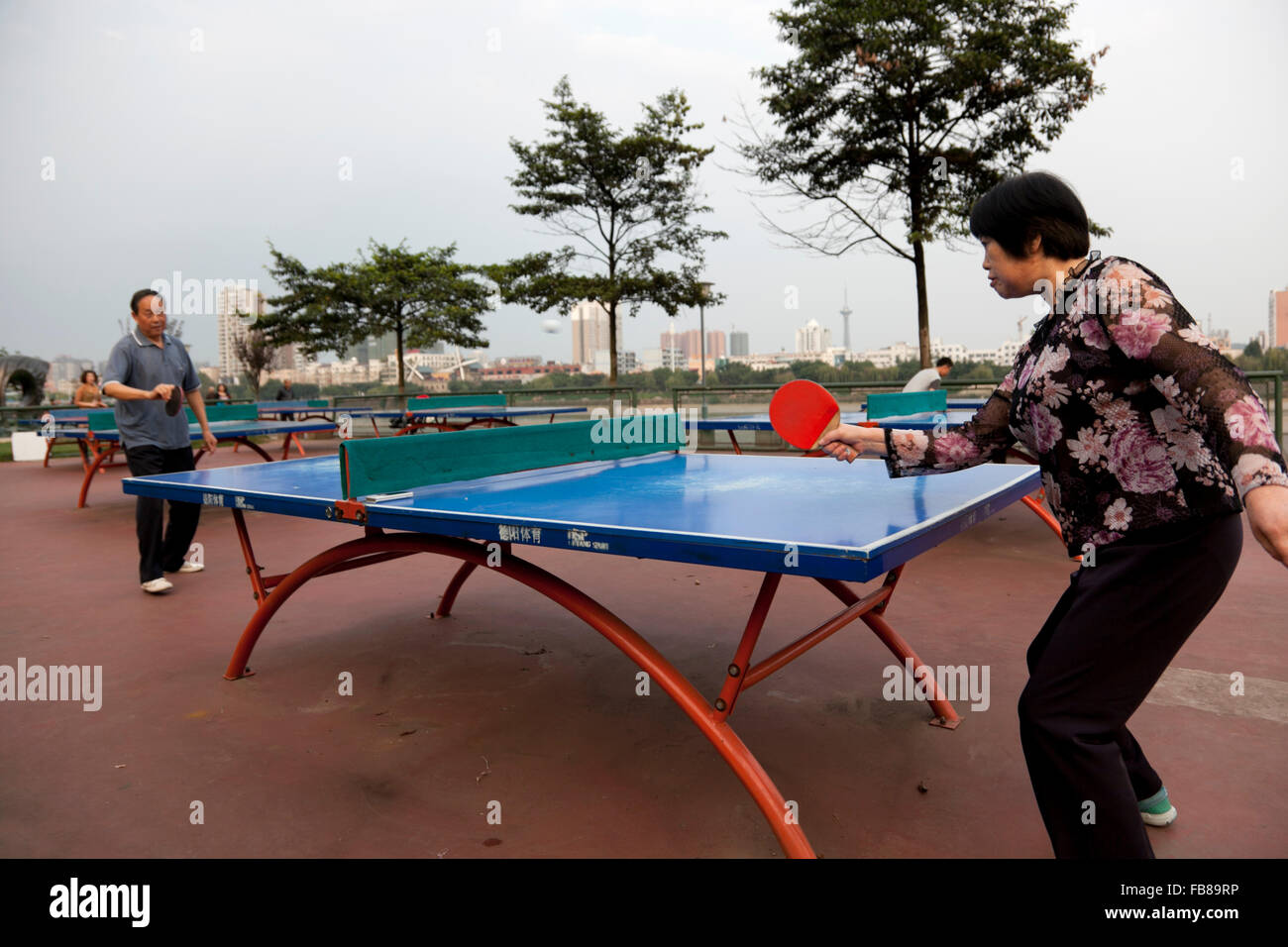 Menschen spielen in einem Park am Flussufer bei einer typischen Stadt in China Tischtennis. Stockfoto