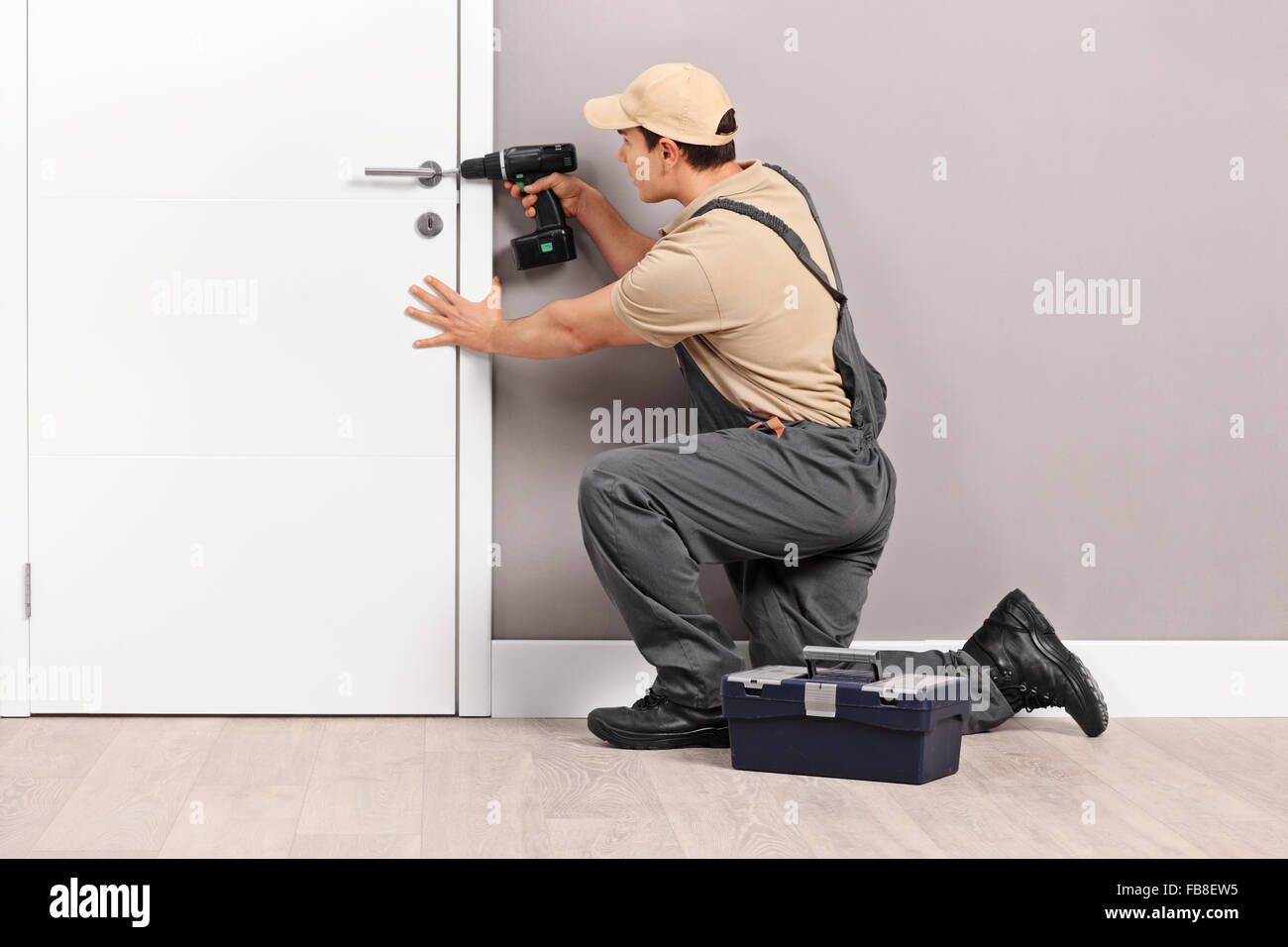 Junge männliche Schlosser Installation eine Sperre auf eine neue weiße Tür mit einer Handbohrmaschine Stockfoto