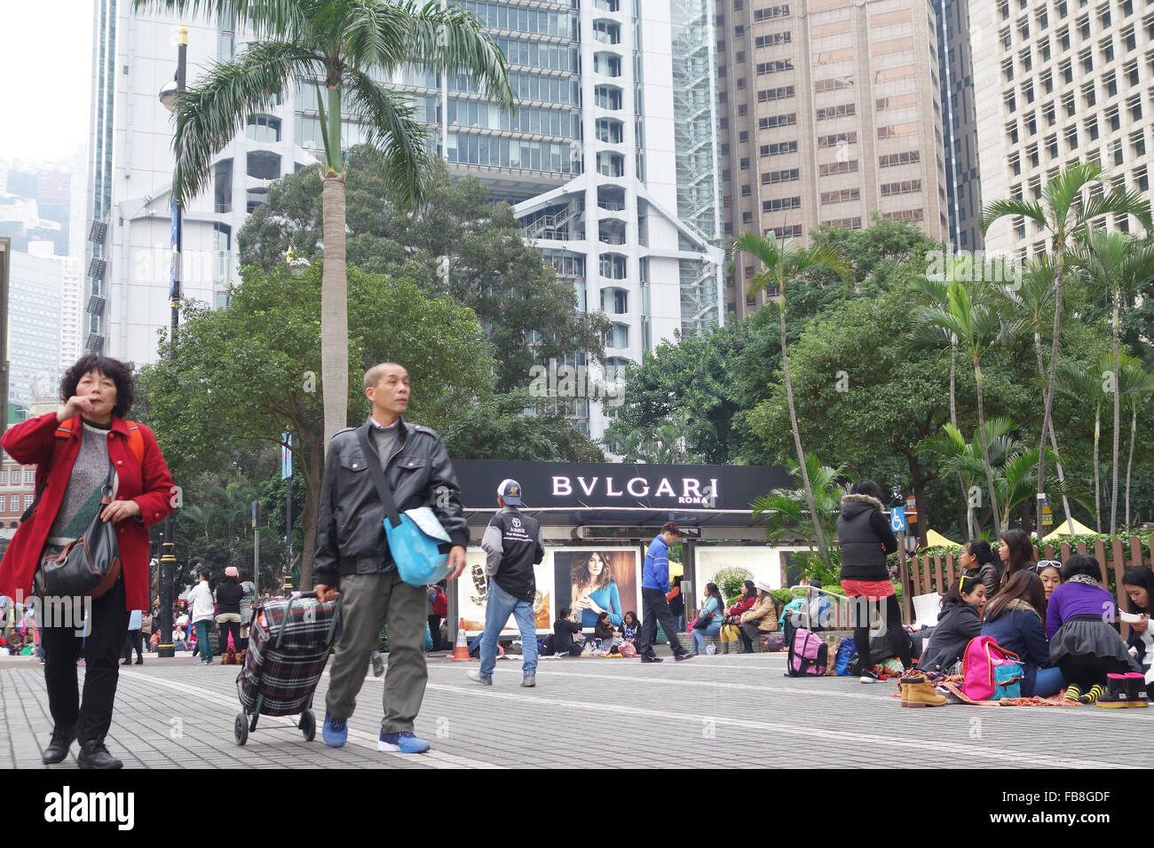 Ein paar Spaziergänge durch den wichtigsten Geschäftsviertel in der Nähe der Statue Square in Hong Kong, China, 20. Dezember 2015. Jeden Sonntag wird ein Treffpunkt für Tausende von philippinischen Hausangestellten Stadtteil verwandelt. Das Arbeitnehmer-Picknick auf dem Boden, Karten spielen, tanzen, halten Schönheitswettbewerbe oder ruhen neben Banken und Mode Poster. Foto: ANNE-SOPHIE GALLI/dpa Stockfoto