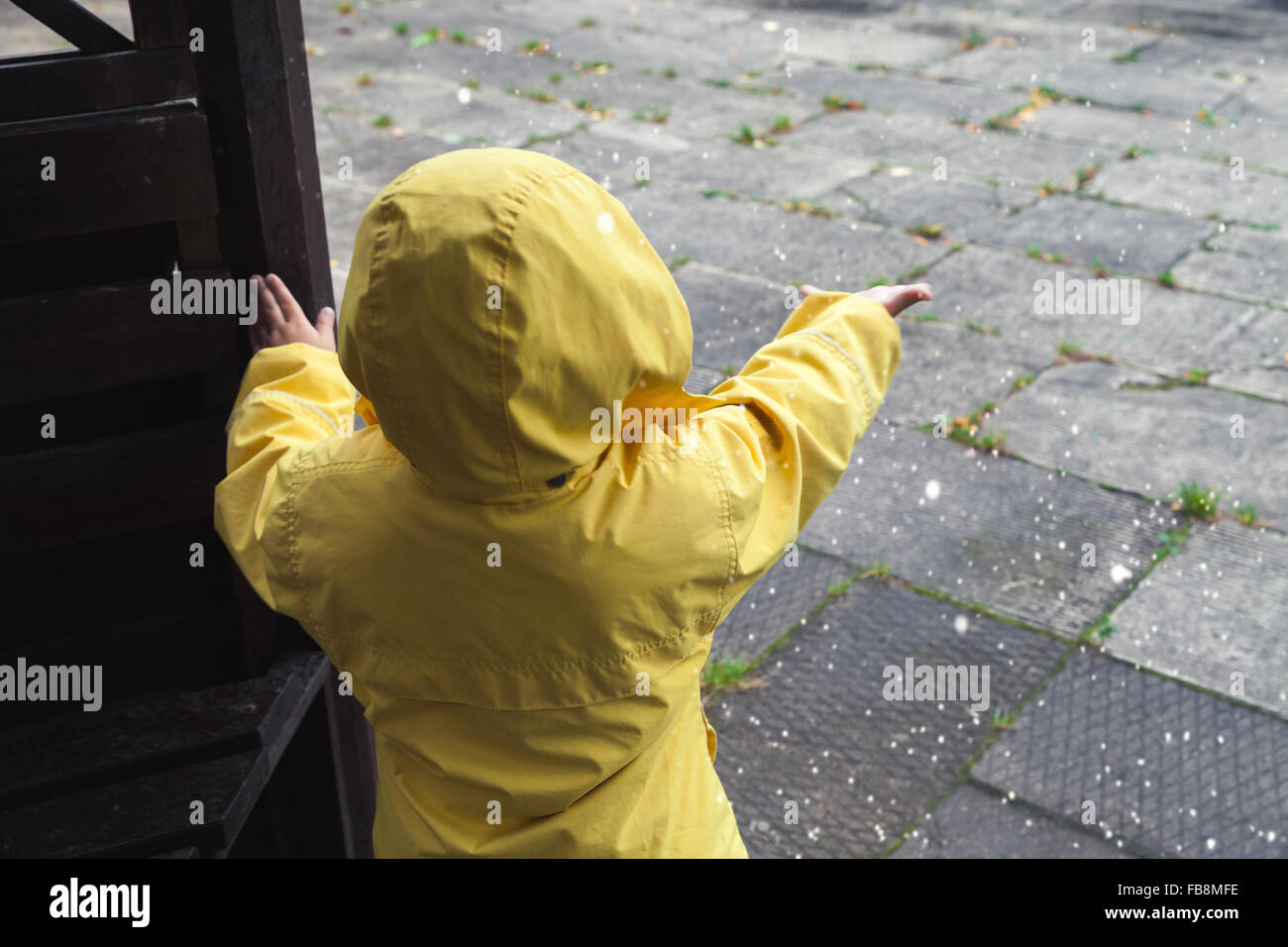 Kleines Kind im gelben Regenmantel mit Wasser spielen fällt Stockfoto