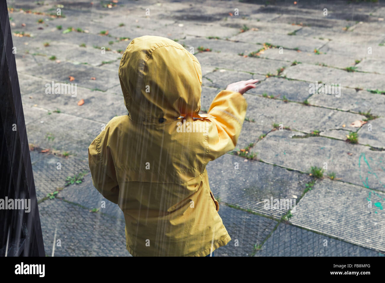 Kleines Kind im gelben Regenmantel mit Regentropfen zu spielen. Vintage Tonwertkorrektur-Foto-Filter-Effekt Stockfoto