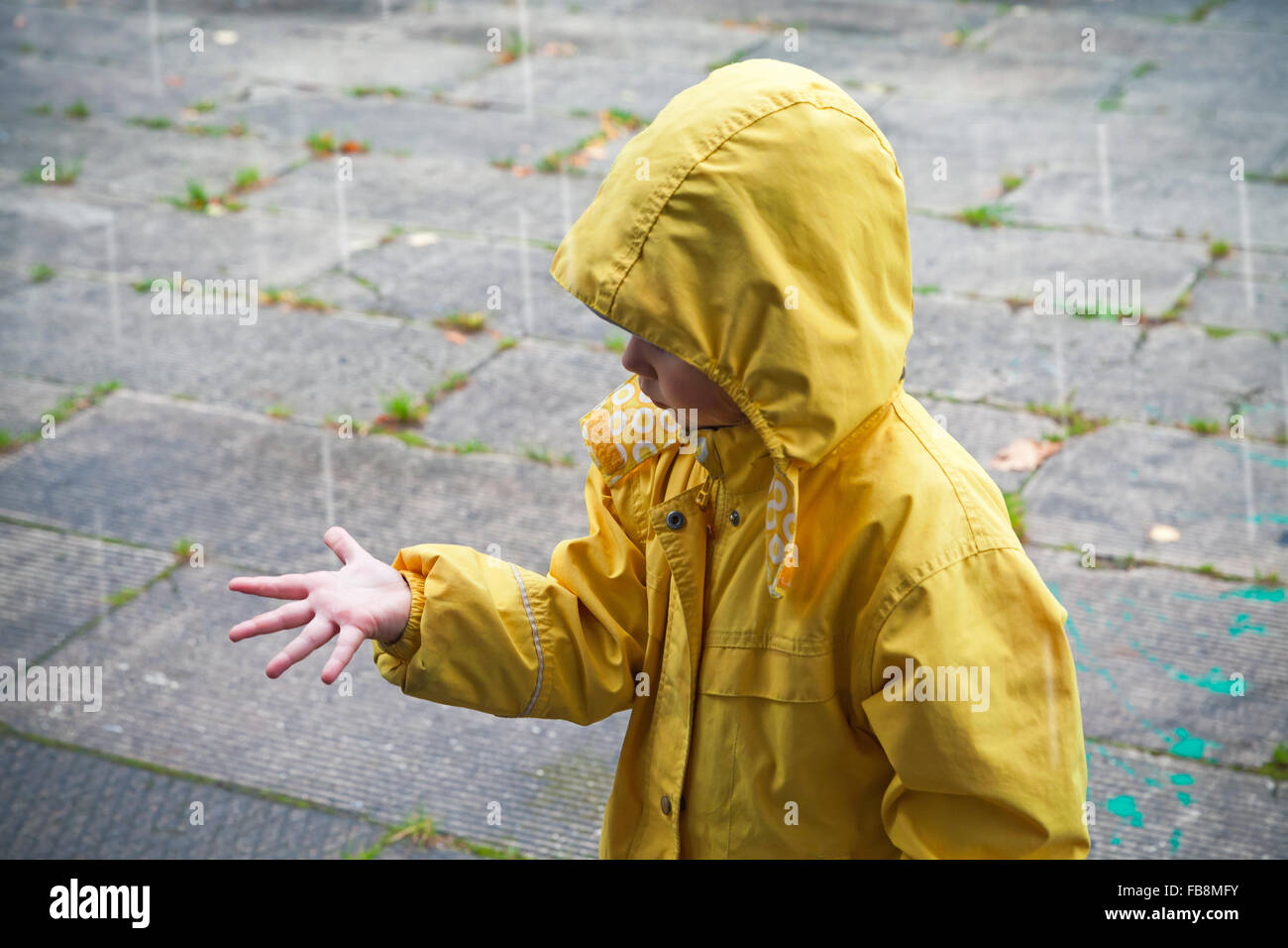 Kleines Kind im gelben Regenmantel mit Regentropfen spielen Stockfoto