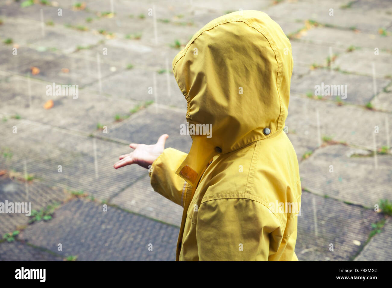 Kleines Kind im gelben Regenmantel mit Regentropfen zu spielen. Vintage stilisierte Tonwertkorrektur-Foto-Filter-Effekt Stockfoto