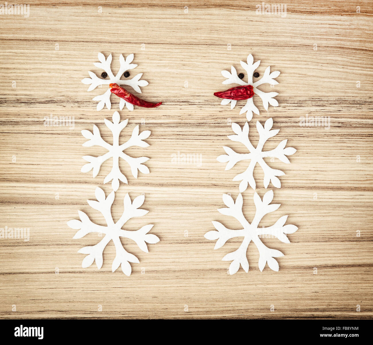 Zwei Schneemänner Schneeflocken und Chilischoten auf dem hölzernen Hintergrund gemacht. Symbol des Winters. Stockfoto