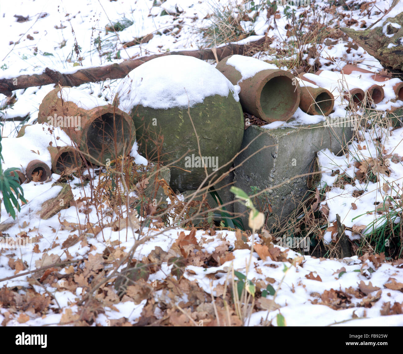Alten Drainagerohre und eine steinerne Kugel als Ornamente in einem verschneiten Winter-Garten Stockfoto