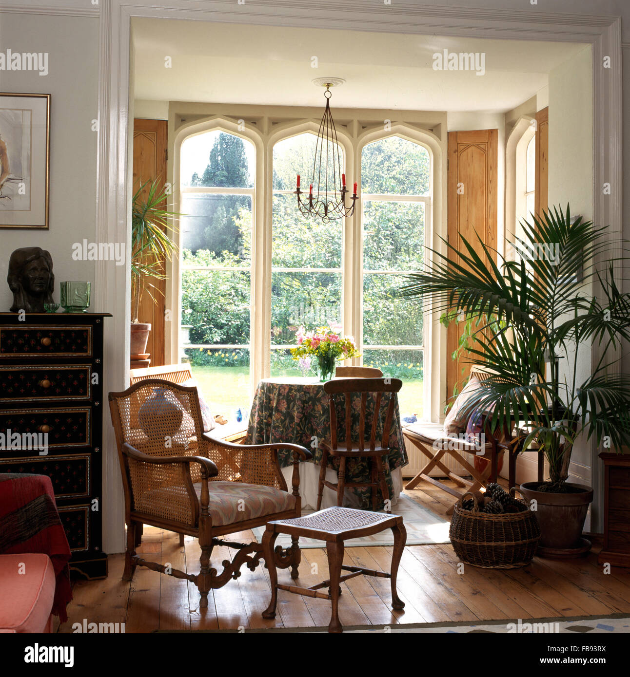 Bergere Sessel und Hocker im Land Wohnzimmer mit eingemachten Palm neben Tür, kleine Sitzecke mit hohen Fenstern Stockfoto