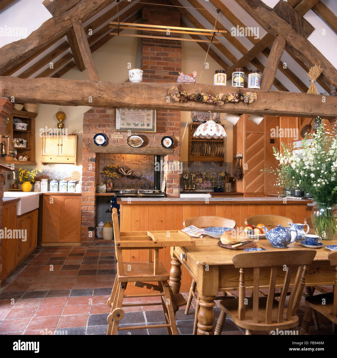 Holzstühle und Kinderhochstuhl am Kiefer Tisch im Stall Umbau Küche mit rustikalen Holzbalken Stockfoto
