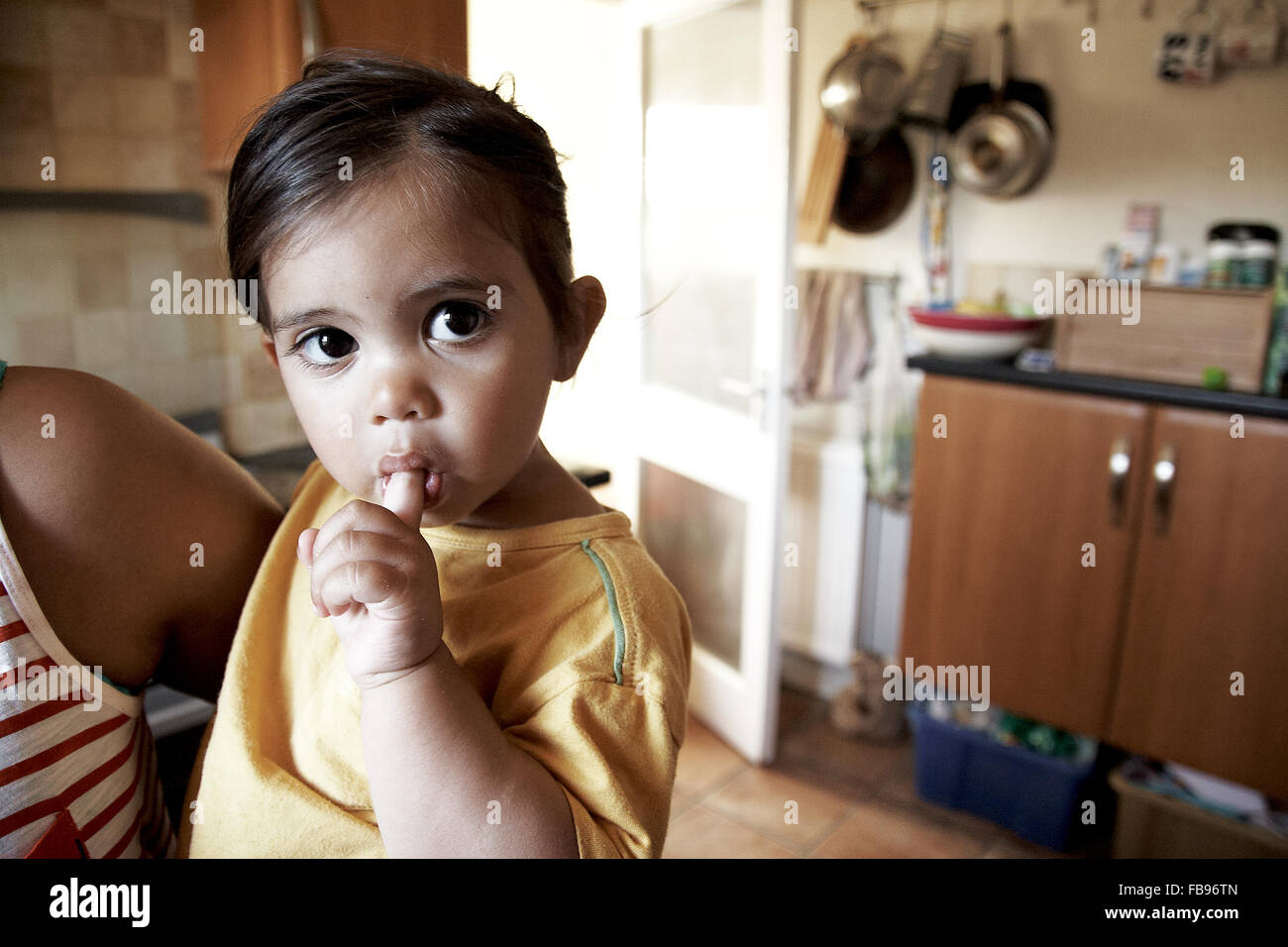 Gemischte Rassen Kleinkind Mädchen saugt den Finger in der Küche Stockfoto