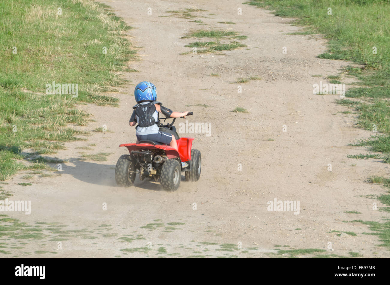 Jungen mit dem roten ATV Quad Fahrrad auf einem trockenen Feldweg an einem Sommertag Stockfoto