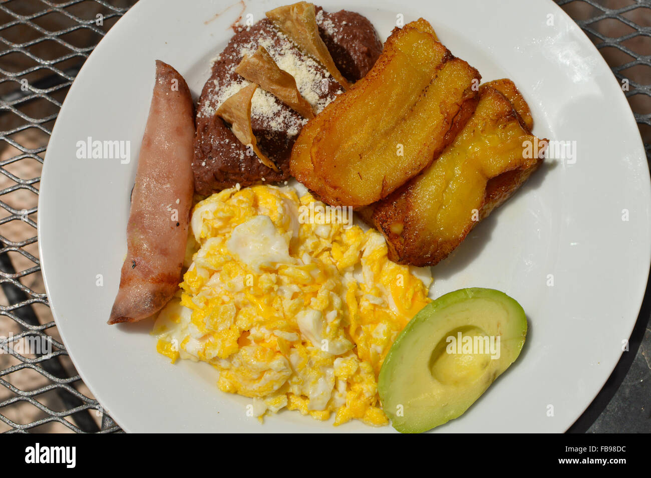 Typische honduranische Frühstück mit Rührei, gebratene Kochbanane, Avocado, gebackenen Bohnen, Tortilla-Chips und Schinken Stockfoto