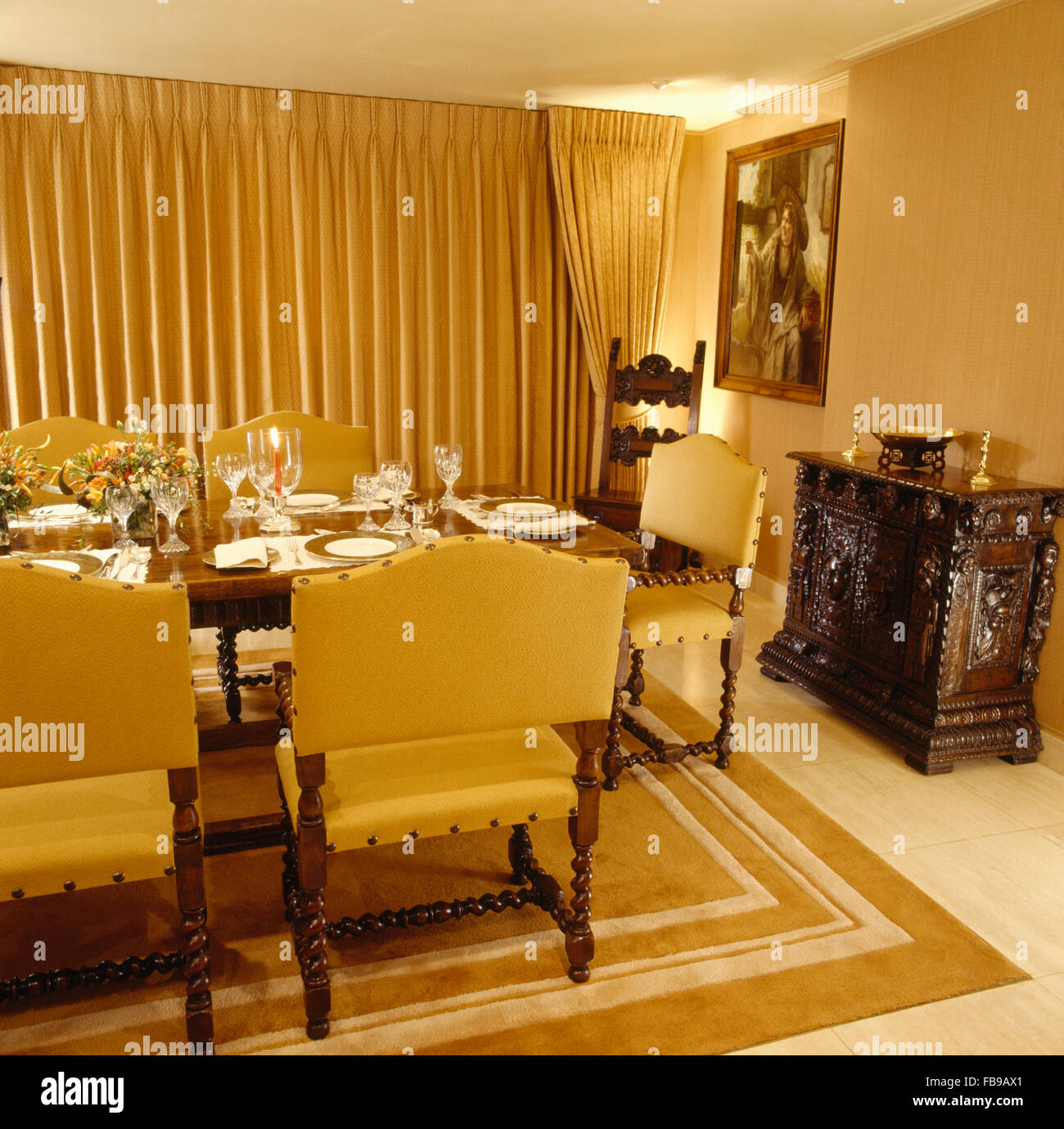 Gelbe Polsterstühle am Tisch für das Abendessen im Esszimmer mit einem geschnitzten hölzernen Sideboard der achtziger Jahre eingestellt und gelber Seide Vorhänge Stockfoto
