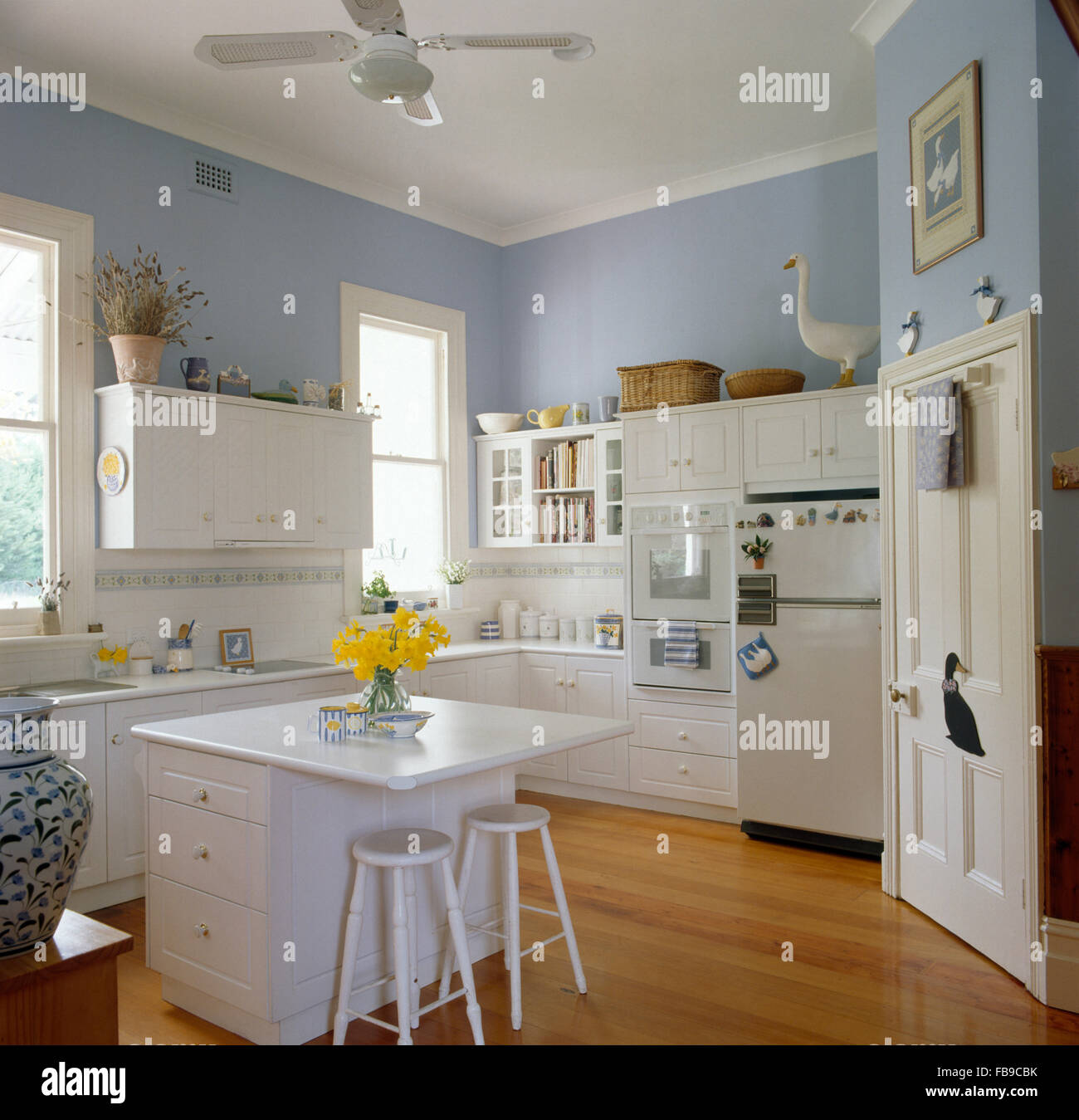 Weißer Hocker an Insel-Einheit in einem blassen Blau Küche mit Holzboden und weiße sind Stockfoto