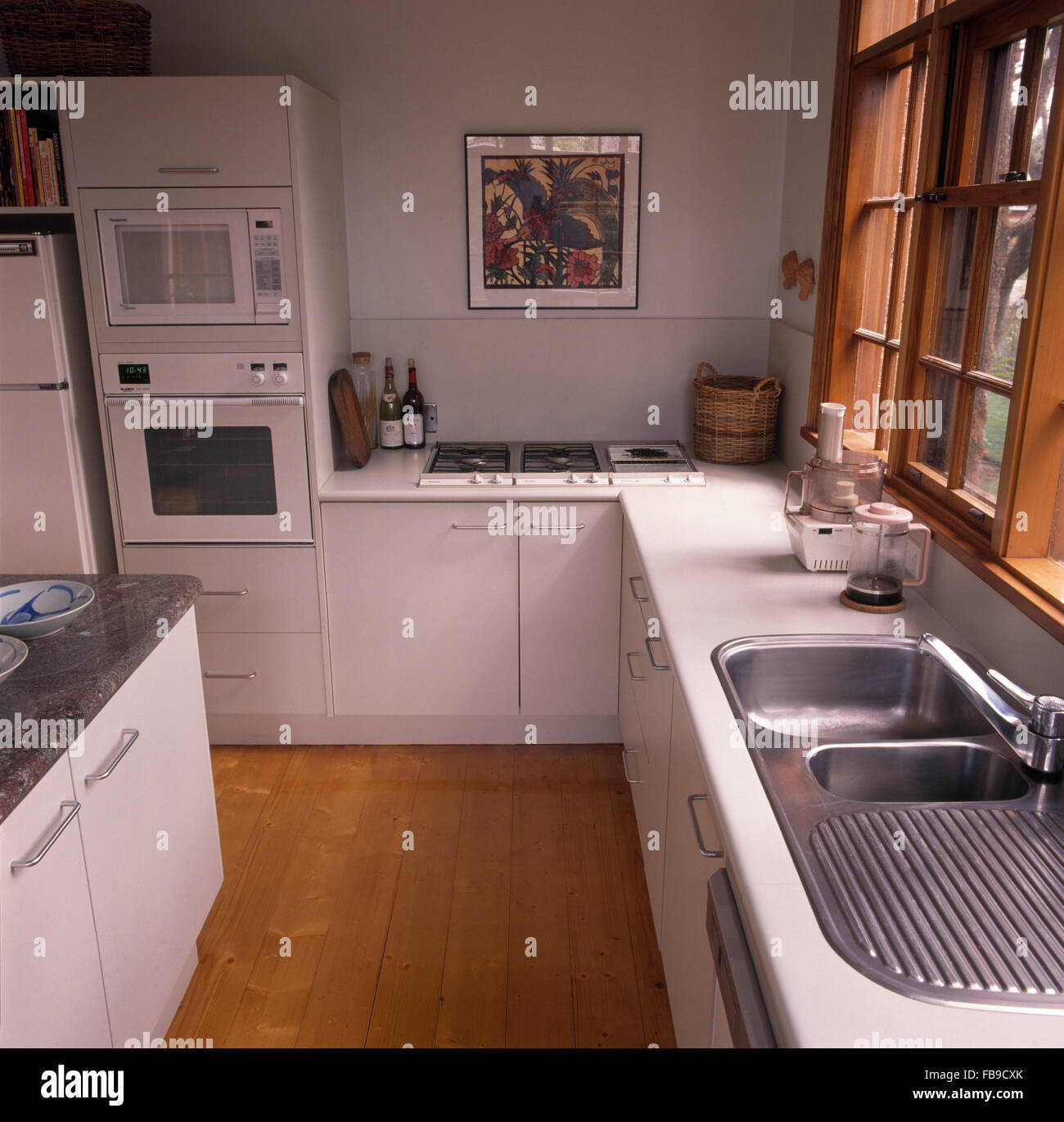 Edelstahl Doppelwaschbecken und Holzböden in eine weiße Küche mit Doppel-Backofen auf Augenhöhe Stockfoto
