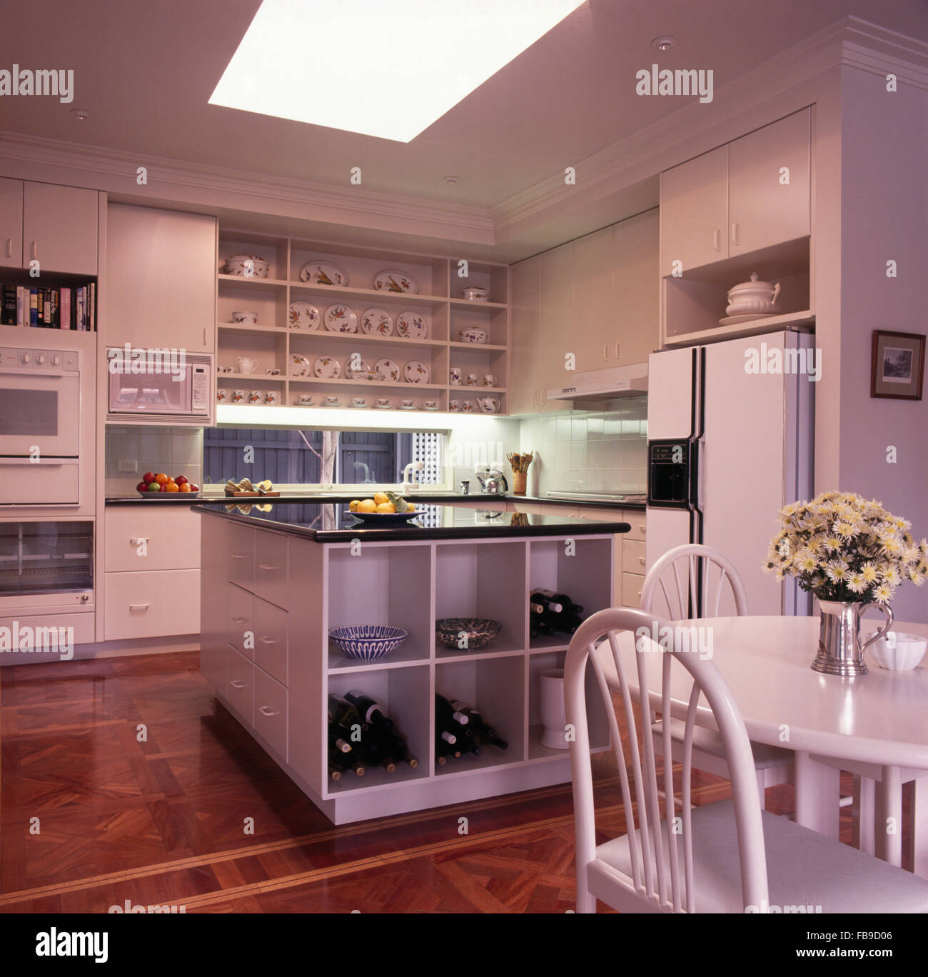 Weißen Esstisch und Stühlen und ein amerikanisches Kühlschrank mit Gefrierfach in eine weiße Küche mit offenen Cube Regale in Insel Einheit Stockfoto
