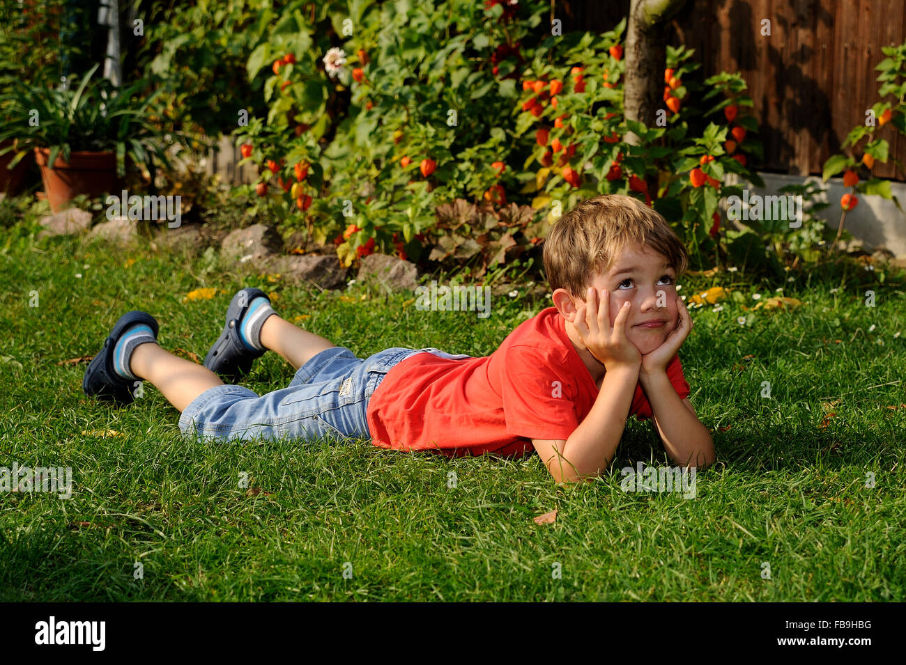 Junge liegend auf dem Rasen, ruhen Kopf in Händen, nachdenklichen Blick Stockfoto