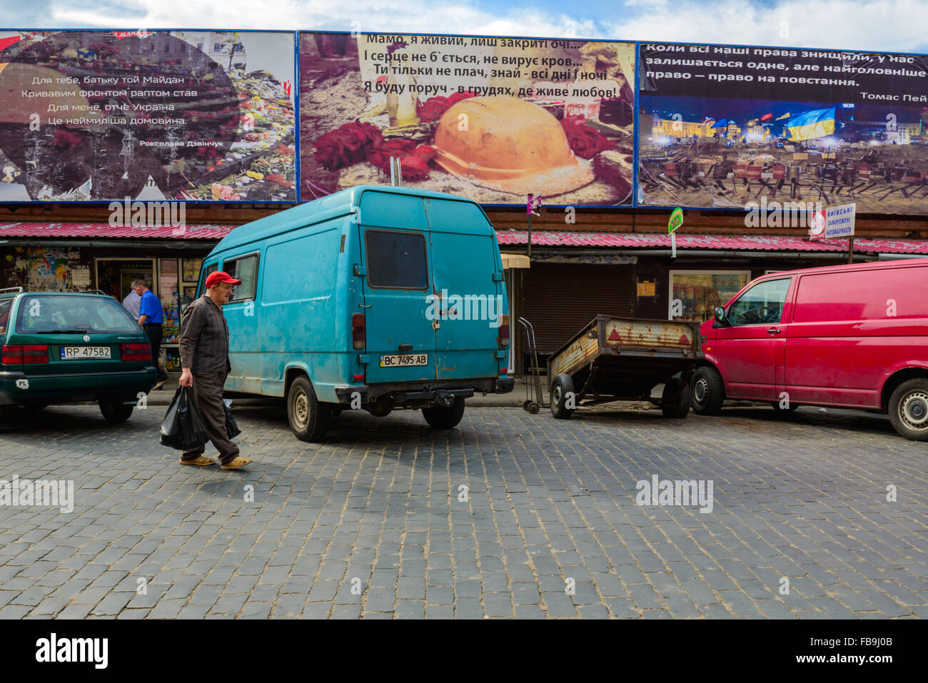 Mann mit Plastiktüte vorbei an Autos und Maydan-Themen Plakatwänden in einem Markt, Lviv, Ukraine Stockfoto