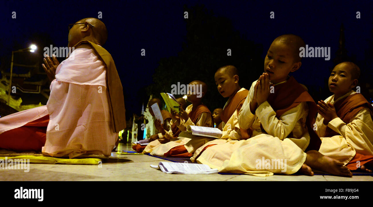 Junge Nonnen singen aus einem Gebet-Buch während der Dämmerung an der Shwedagon Pagode Yangon Myanmar. Stockfoto