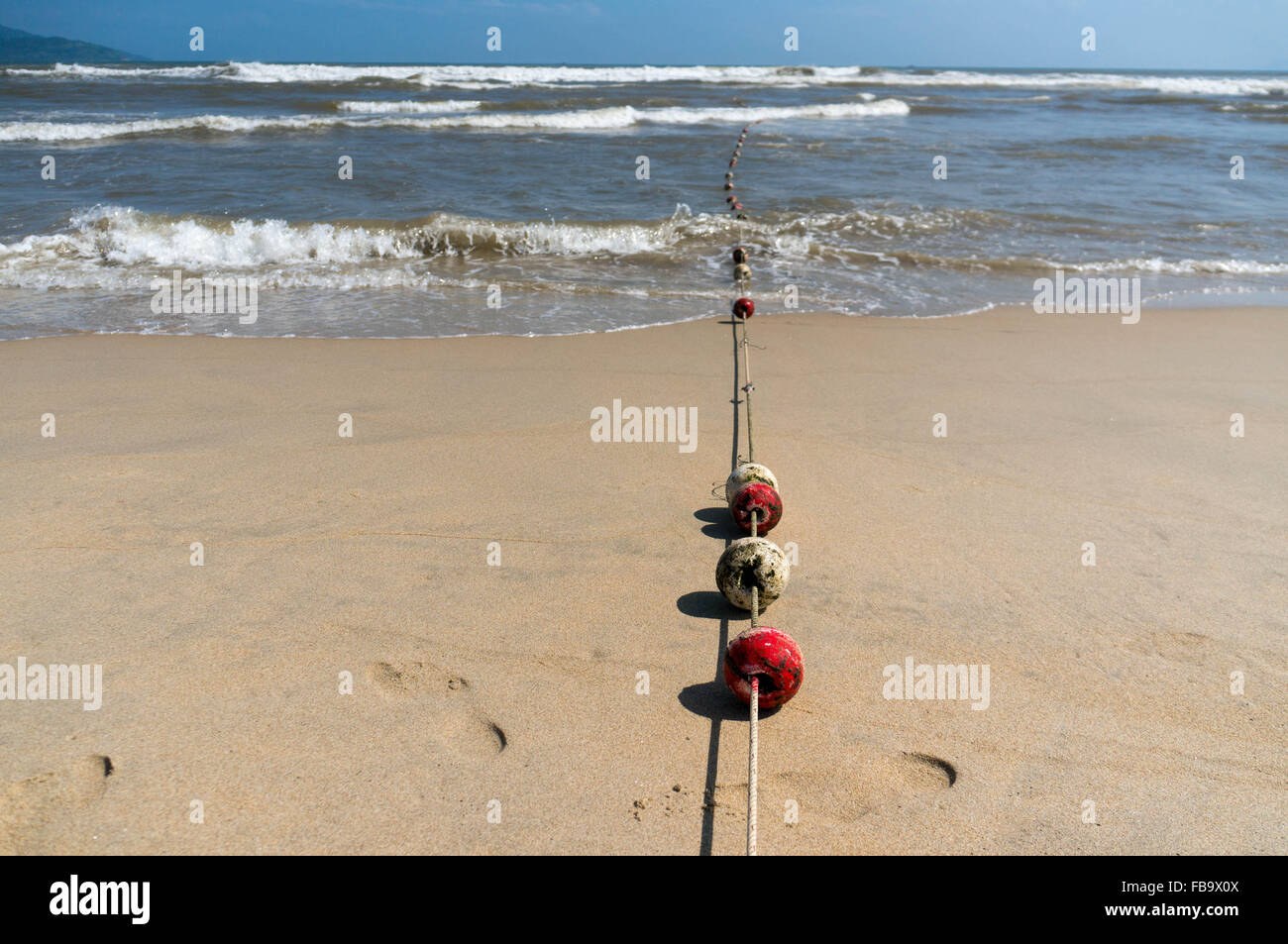 Roten und weiße Bojen an einem Seil führen in den Ozean in Da Nang, Vietnam. Wellen stürzen im Hintergrund. Stockfoto