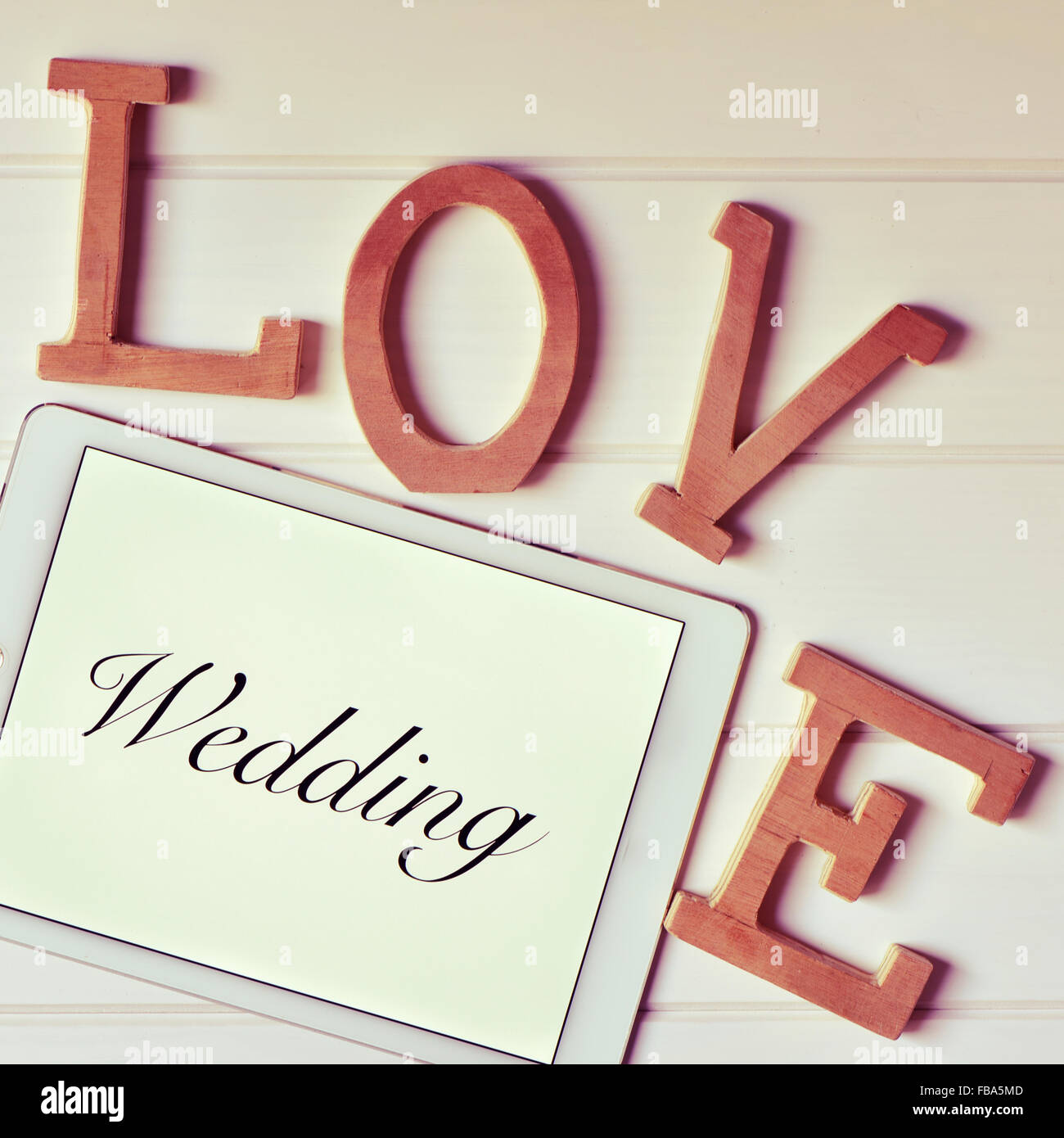 einige hölzerne dreidimensionale Buchstaben bilden das Wort Liebe und ein Tablet-Computer mit dem Wort Hochzeit in seinem Bildschirm auf einem weißen Stockfoto