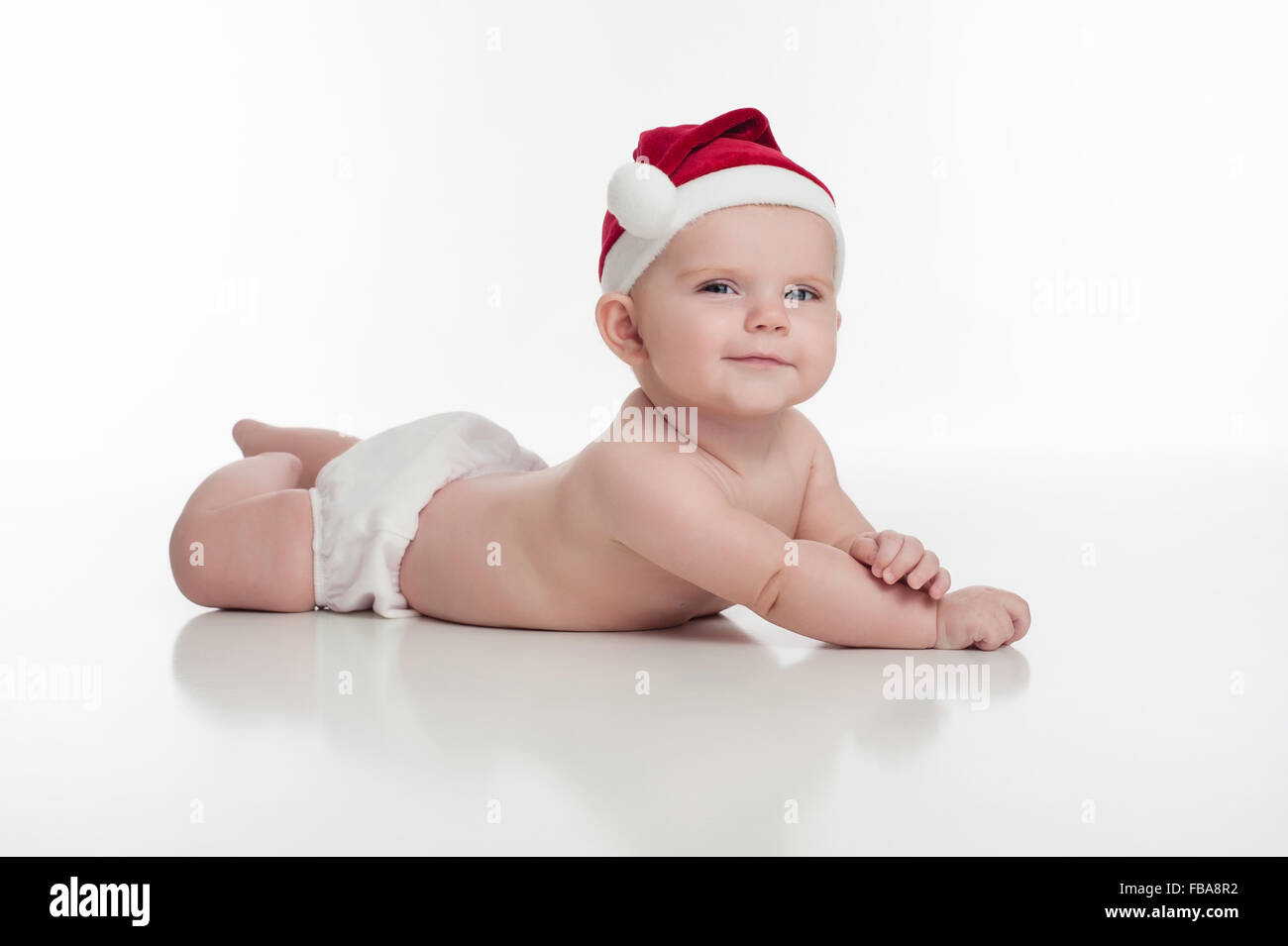 Ein Porträt von einem lächelnden, vier Monate altes Babymädchen tragen eine Weihnachtsmütze und weiße Windel. Sie liegt auf ihrem Bauch, gestützt Stockfoto