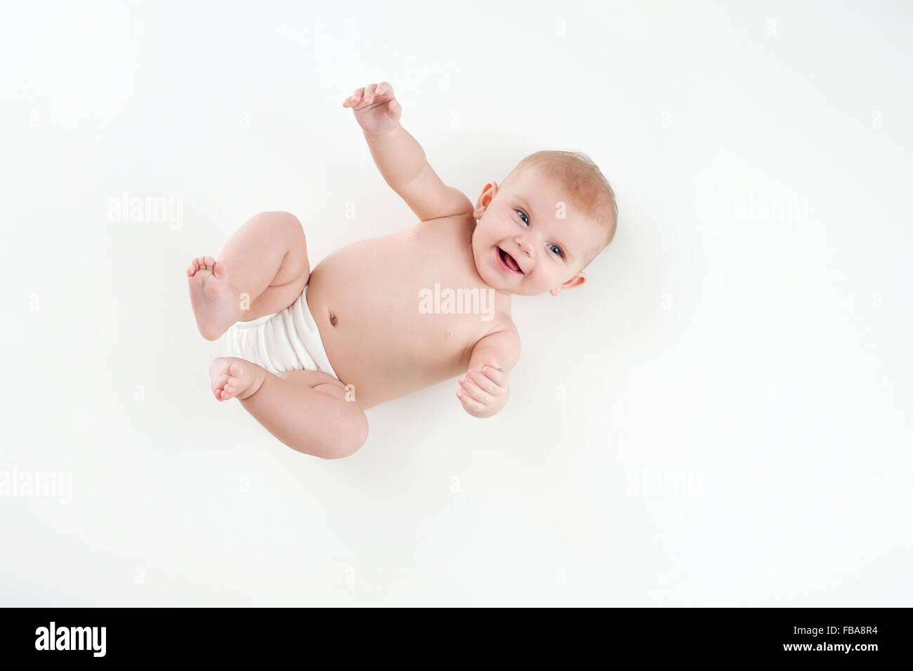 Einem lachenden vier Monate altes baby Mädchen tragen eine weiße Windel decken. Erschossen von oben auf einem weißen Hintergrund. Stockfoto