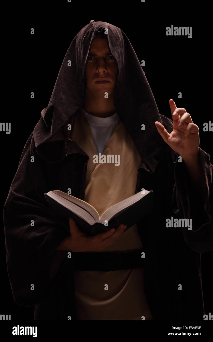 Vertikale Aufnahme eines geheimnisvollen Mönch, der ein Buch hält und Predigt auf schwarzem Hintergrund Stockfoto