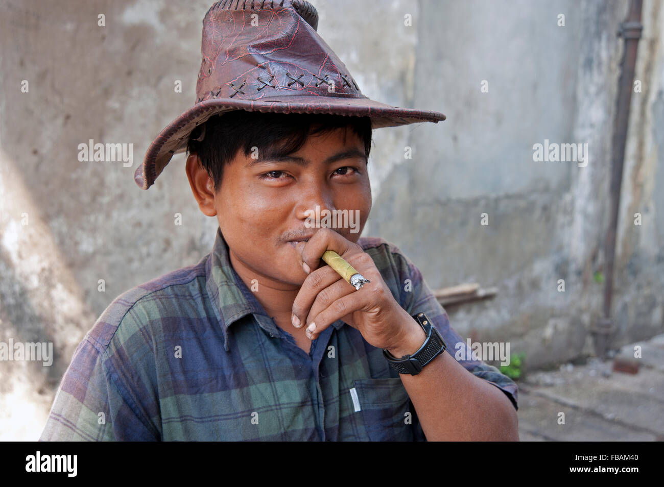 Porträt eines glücklich lächelnde birmanischen mit braunem Leder Hut Rauchen eine burmesische Cheroot eine einfache Steinmauer Yangon Myanmar Stockfoto