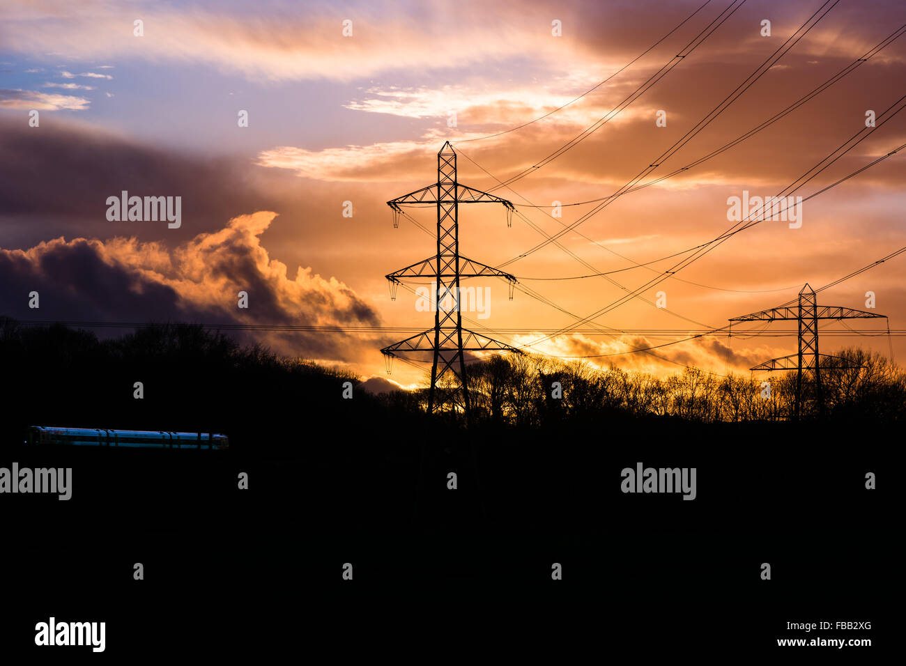 Industrielandschaft mit Kabeln, Zug und Sonnenuntergang. Elektrische Leitungen und Masten sind vor einem Sonnenuntergang Silhouette. Stockfoto