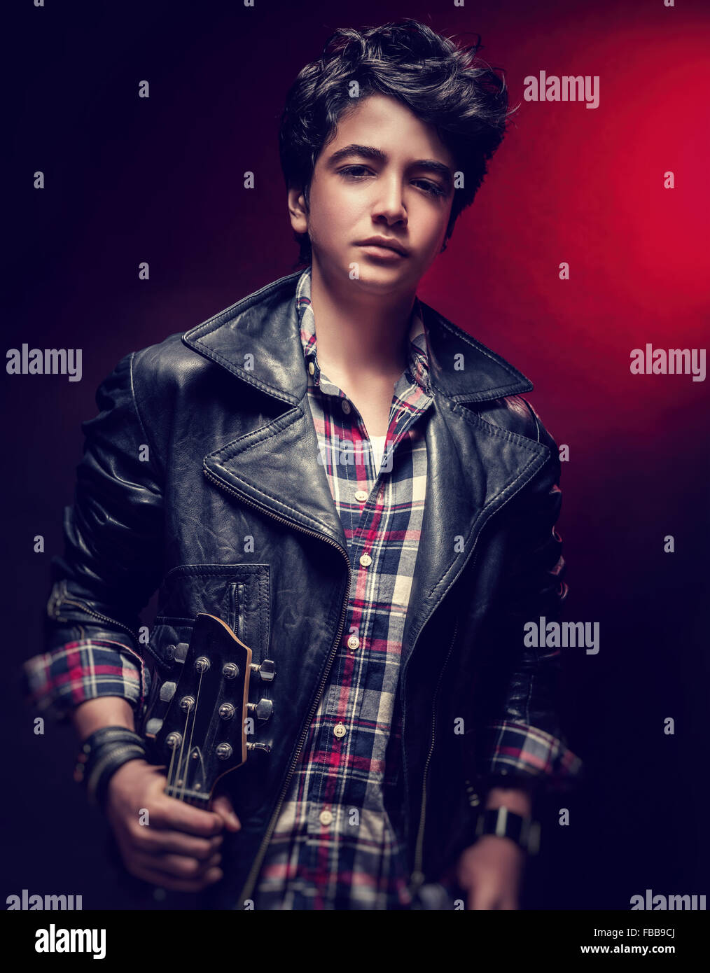 Attraktive Teen Mann posiert mit Gitarre über dunkelroten Hintergrund, Musiker mit modischen Frisur Stockfoto