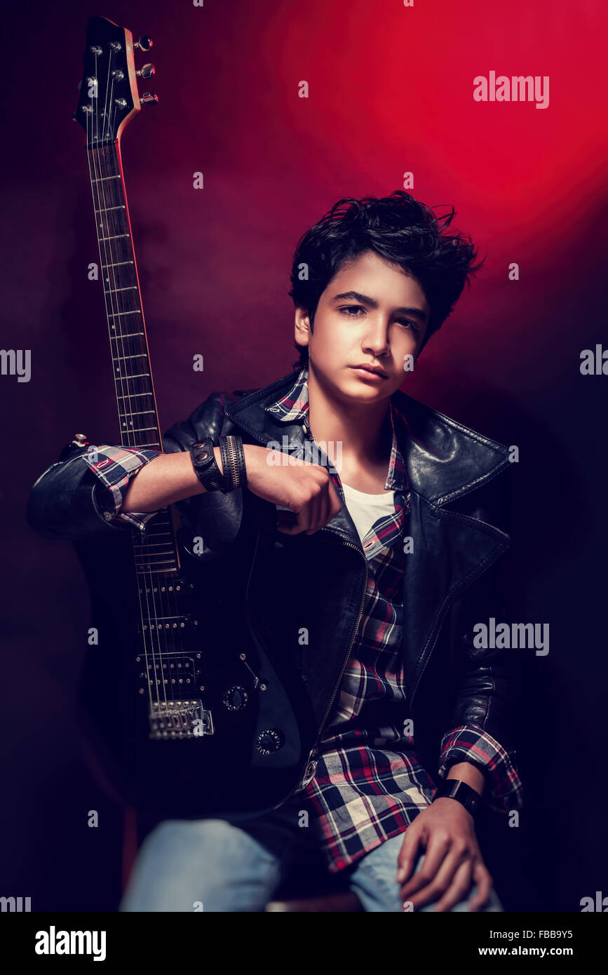 Porträt von hübscher Teen Gitarrist posiert in dunkelroten Hintergrund, tragen trendige Shirt und Ledermantel, coole Teens hobby Stockfoto