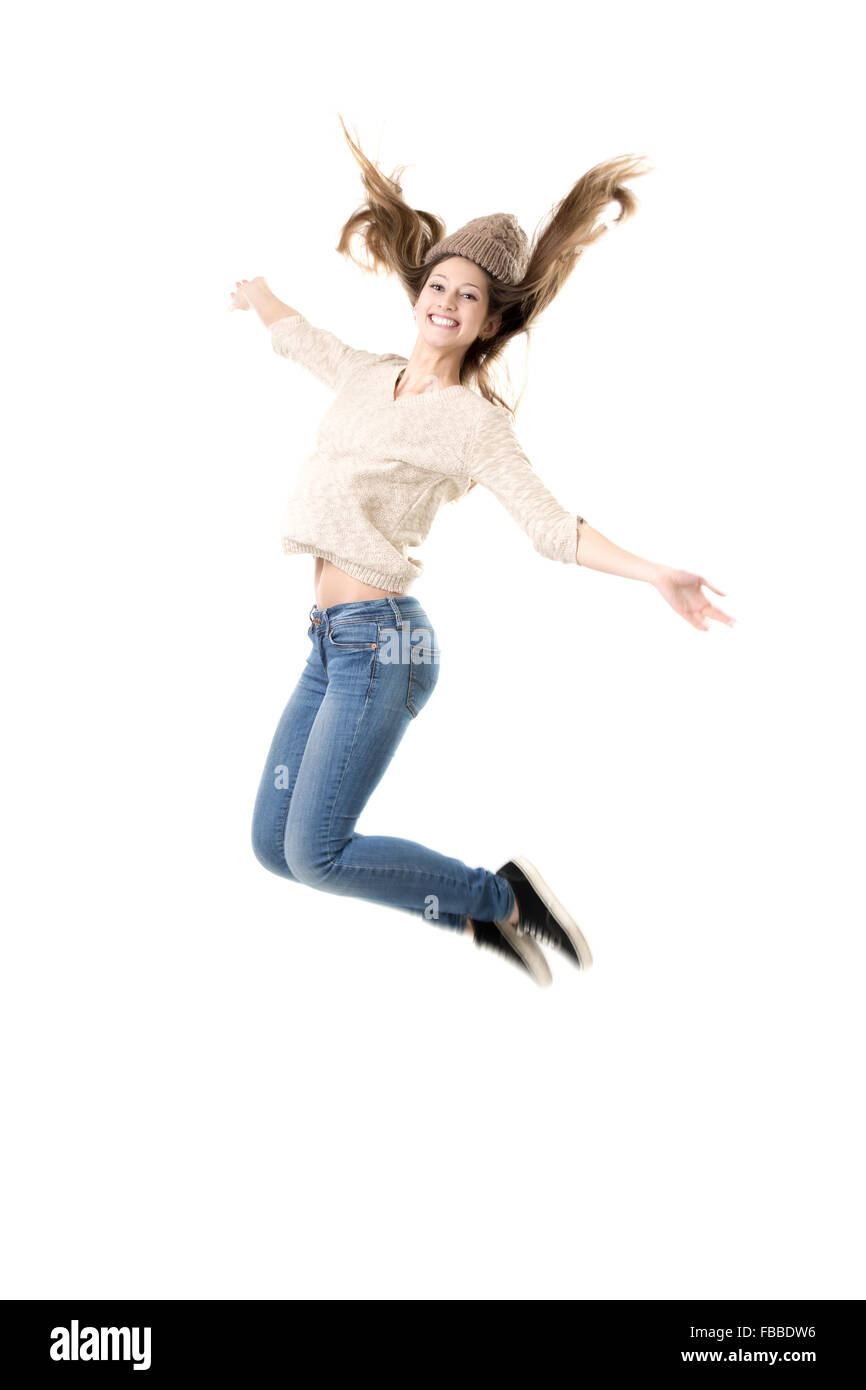 Schöne Teenager-Mädchen mit breiten Lächeln vor Freude springen, tanzen, Jeans, Jersey und Mütze, isoliert Stockfoto