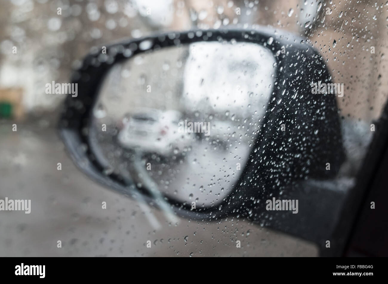 Autofenster mit Regentropfen und Spiegel hinter nass. Nahaufnahme Foto mit Tiefenschärfe und flachen DOF Stockfoto