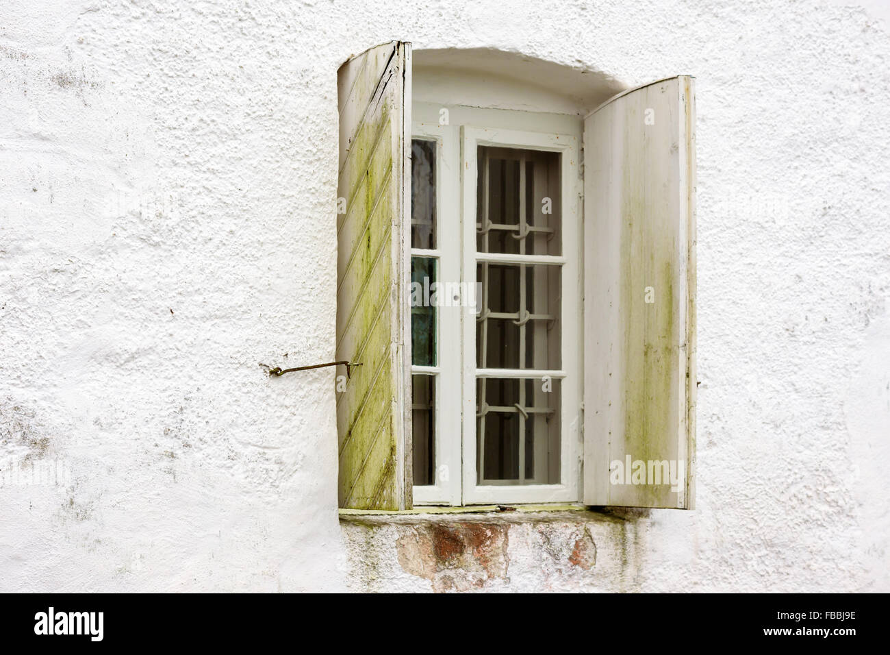 Ein altes Fenster mit Eisenstangen auf die innen und offenen hölzernen Fensterläden auf der Außenseite. Grünes Moos wächst am Rolladen Stockfoto