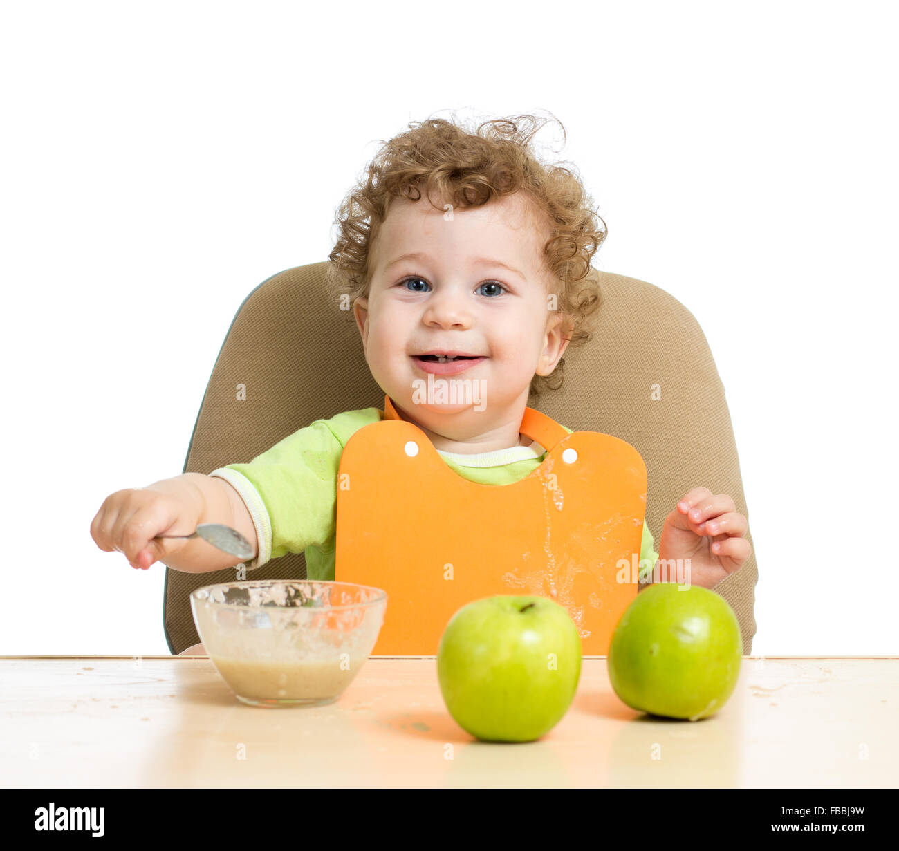kleines Kind isst mit Löffel sitzen am Tisch mit Früchten Stockfoto