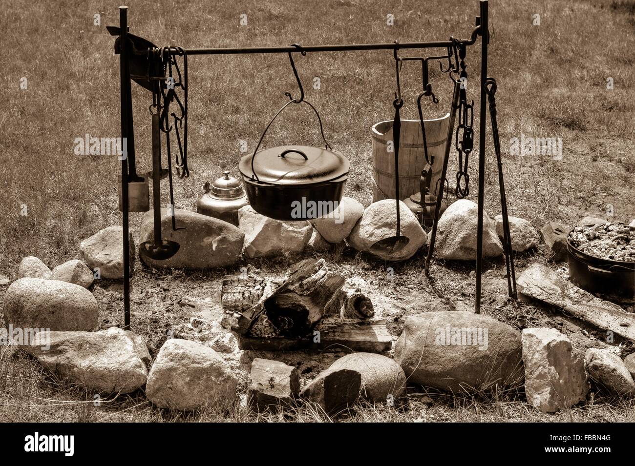 Am Lagerfeuer kochen. Kessel über dem Lagerfeuer mit Pionier Kochutensilien in schwarz und weiß. Stockfoto