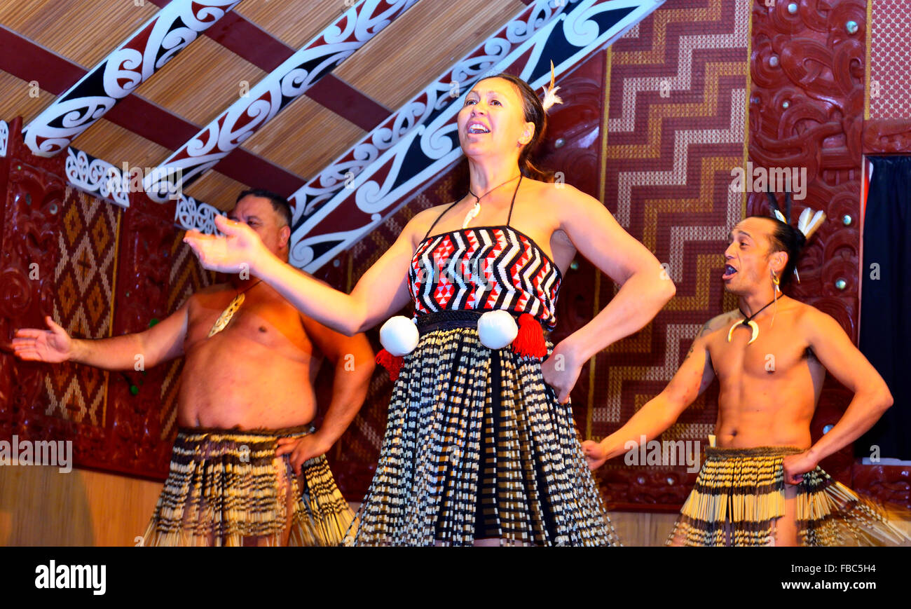 Maori-Frau, die mit Poi(s) um ihre Taille tanzt, während die Männer ihre Bewegungen nachhallten, während eines Maori-Konzertes, Te Puia, Rotorua, Nordinsel, Neuseeland Stockfoto