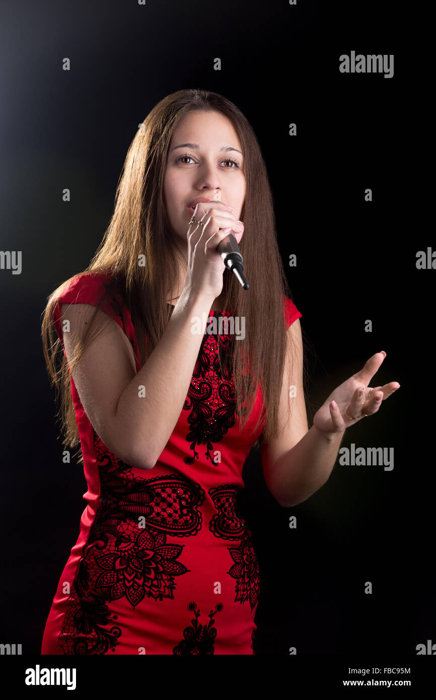 Porträt von schönen Mädchen im roten Kleid leidenschaftlich singen oder handeln mit Mikrofon Stockfoto